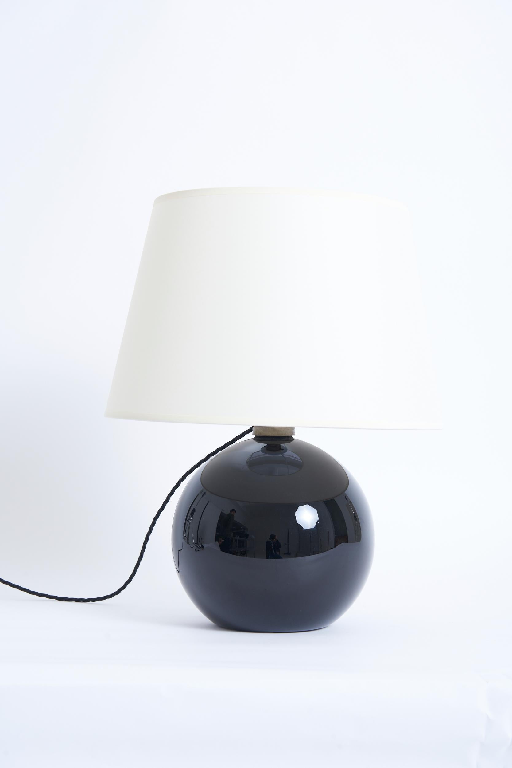 A black opaline glass table lamp attributed to Jacques Adnet (1900-1984). 
France, Circa 1930
With the shade: 51.5 cm high by 40.5 cm diameter 
Lamp base only: 33 cm high by 25 cm diameter 