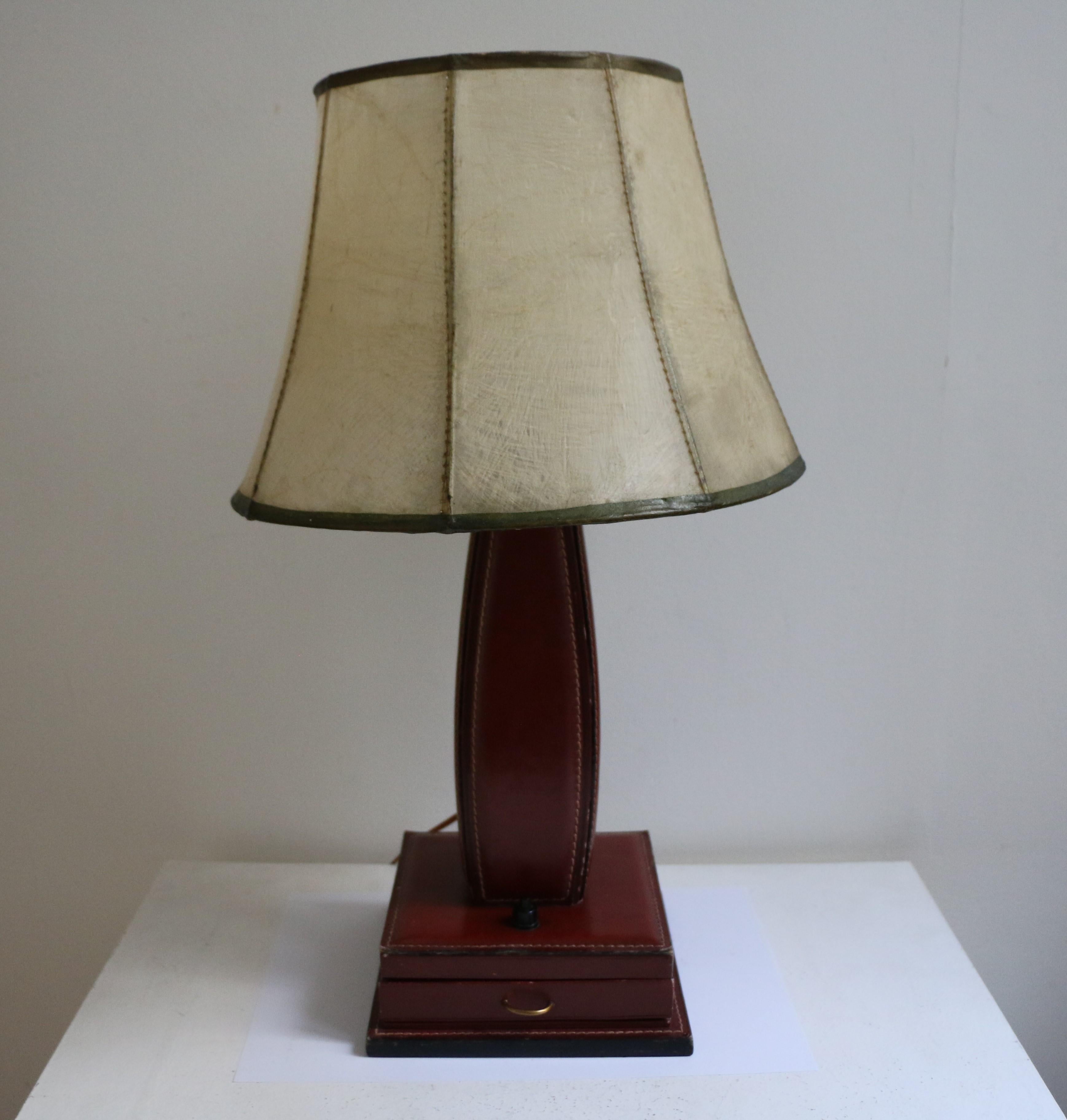 Table lamp by Jacques Adnet with red stitched leather entirely covering a wood structure. Square base with a small drawer (brass handle). Shade is original and made fiberglass on metal thread. Wired for European use.
Dimensions:
- Base: H 33cm, L