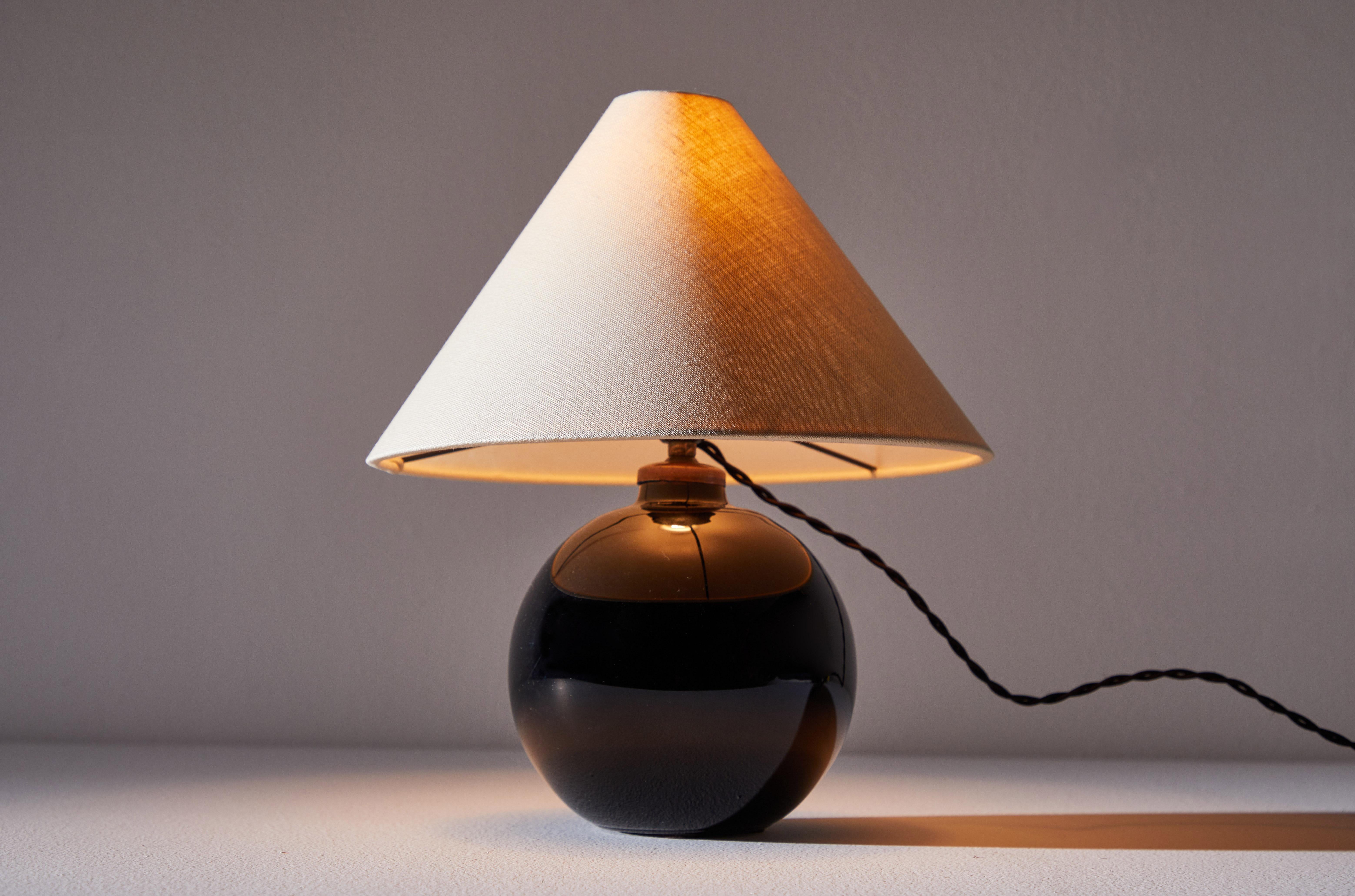 Spherical table lamp by Jacques Adnet. Designed and manufactured in France, circa 1930s. Original glass, brass and custom natural linen shade. Rewired for U.S. standards with French twist silk cord. This fixture has one socket. We recommend one