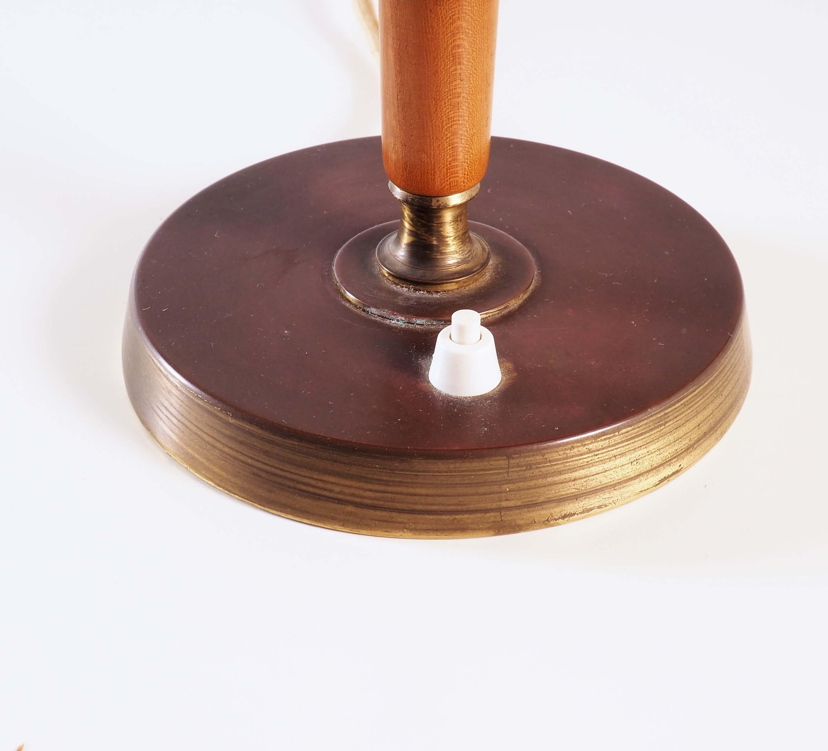 Table lamp made during the 1940s for Stockholms leading warehouse Nordiska Kompaniet at their own factory in Nyköping. The lamp base is in brass and elm. The inner-shade is in glass and the outer shade is in painted metal.