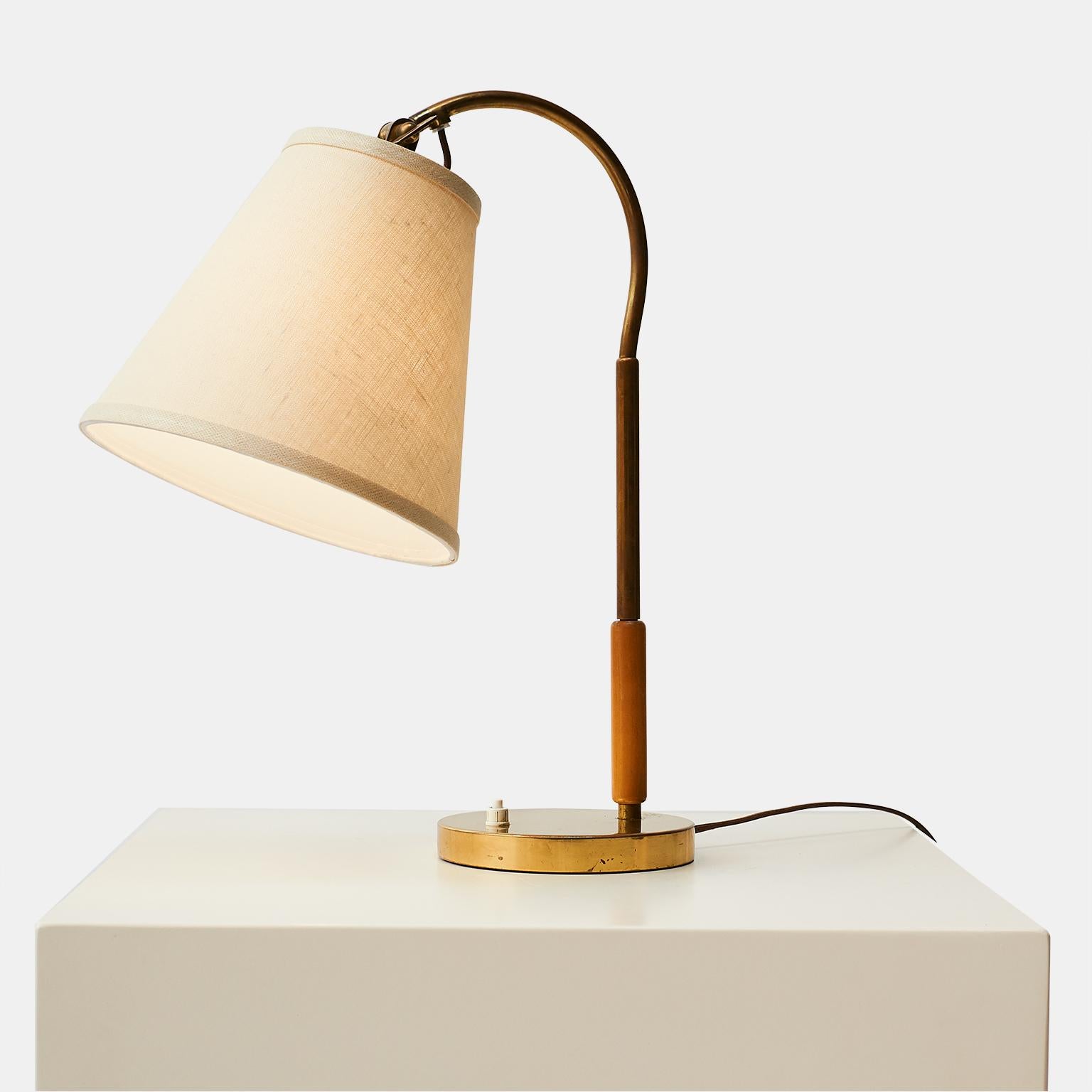 An elegant table lamp with brass base, and elmwood on the body. Designed by Paavo Tynell. 

The lamp features a new shade, new light bulb socket, new wiring.