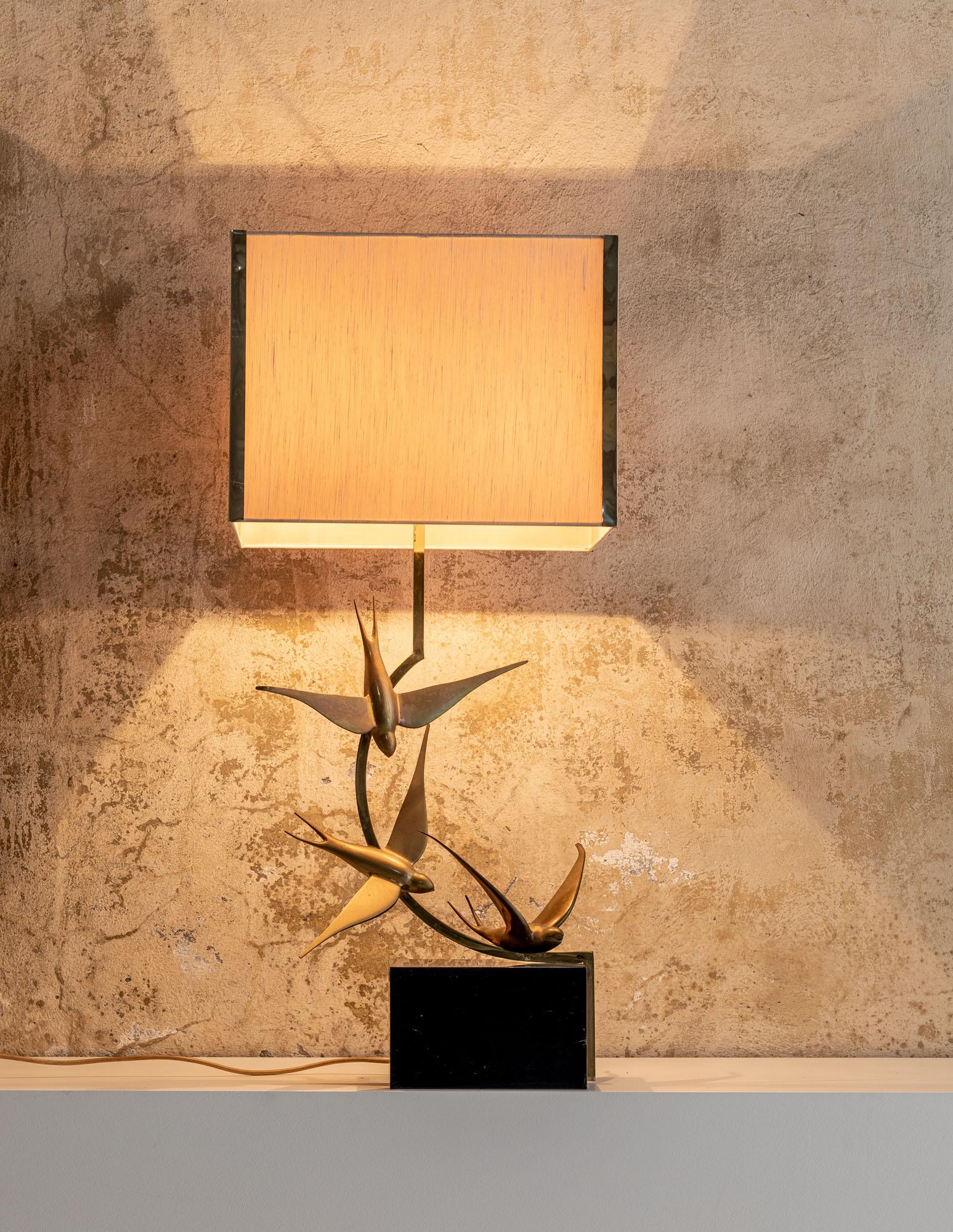 Table lamp in solid brass. The base is composed by a cubic element and three swallows.
Original squared light brown lamp shade with brass details. The lamp is signed on the base.