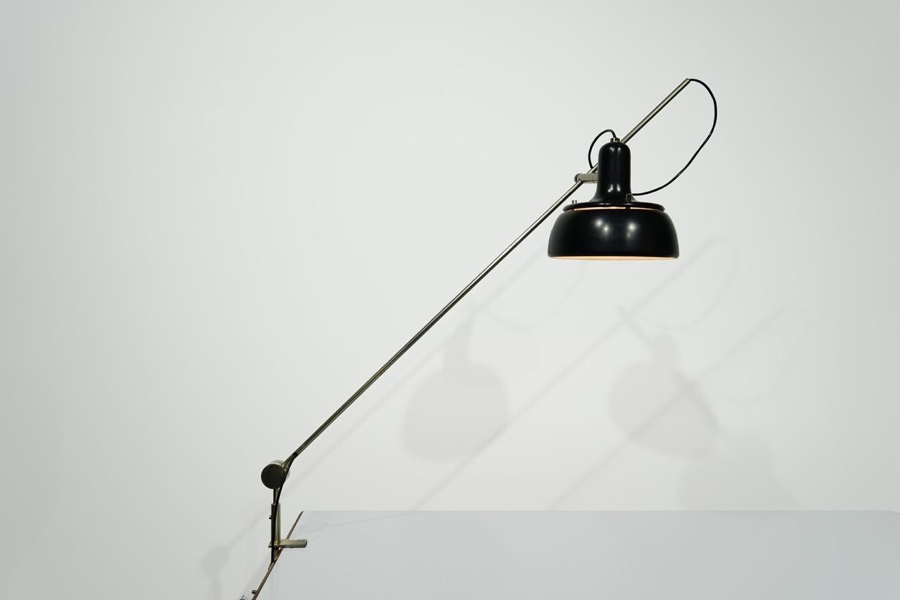 Verstellbare Stahl Schreibtischlampe alle, schwarz lackiertem Aluminium-Reflektor.
Hersteller: O-Luce.

* 
Tito Agnoli wurde 1931 in einer italienischen Familie in Lima, Peru, geboren. Nach dem Krieg kam er nach Italien. Ausgebildet als Maler