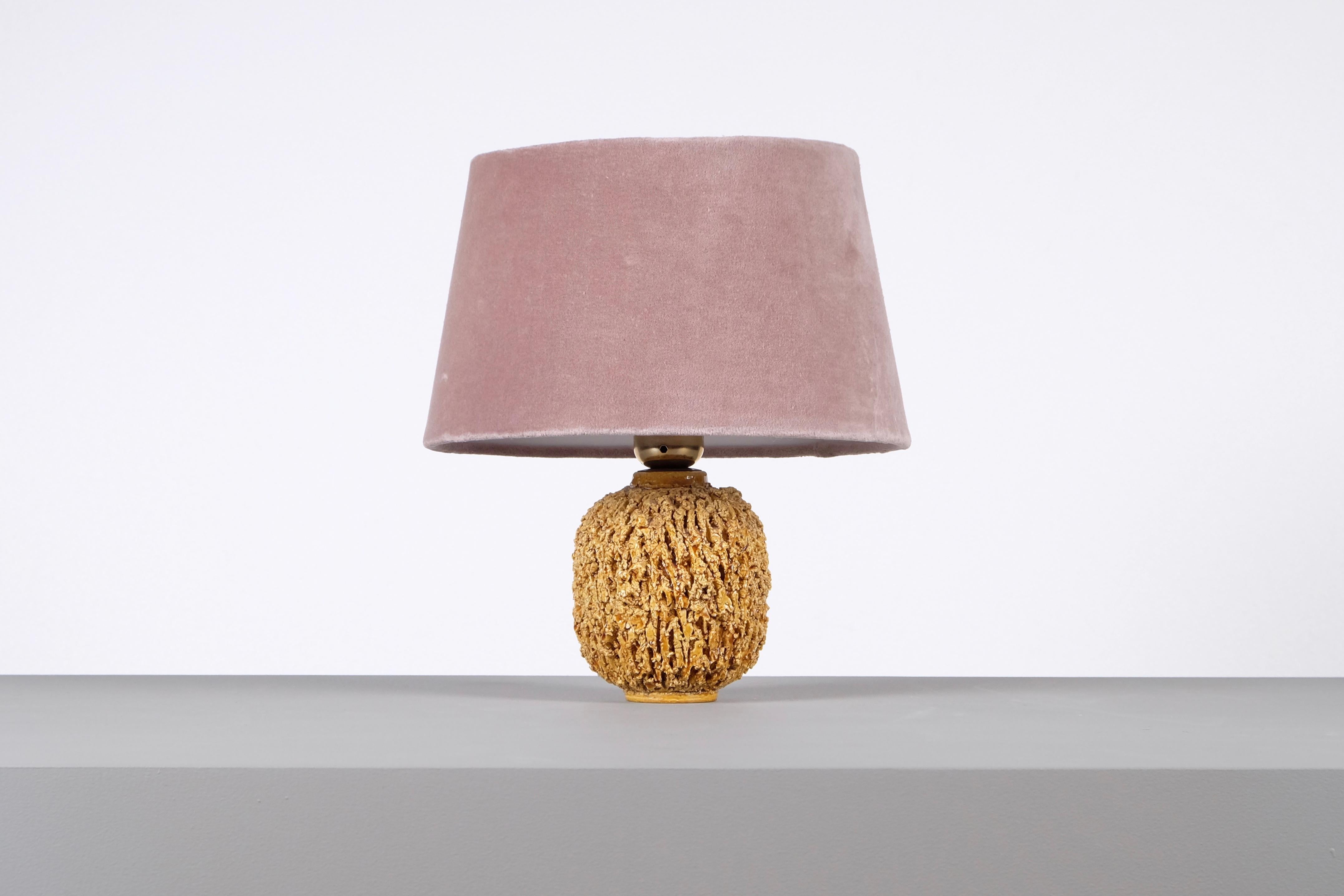 Ceramic lamp in bulbous shape by Gunnar Nylund, composed of chamotte clay and glazed with a gold colored luster glaze. Produced by Rörstrand. 
Stamped. Height including shade: 28 cm. New wiring.