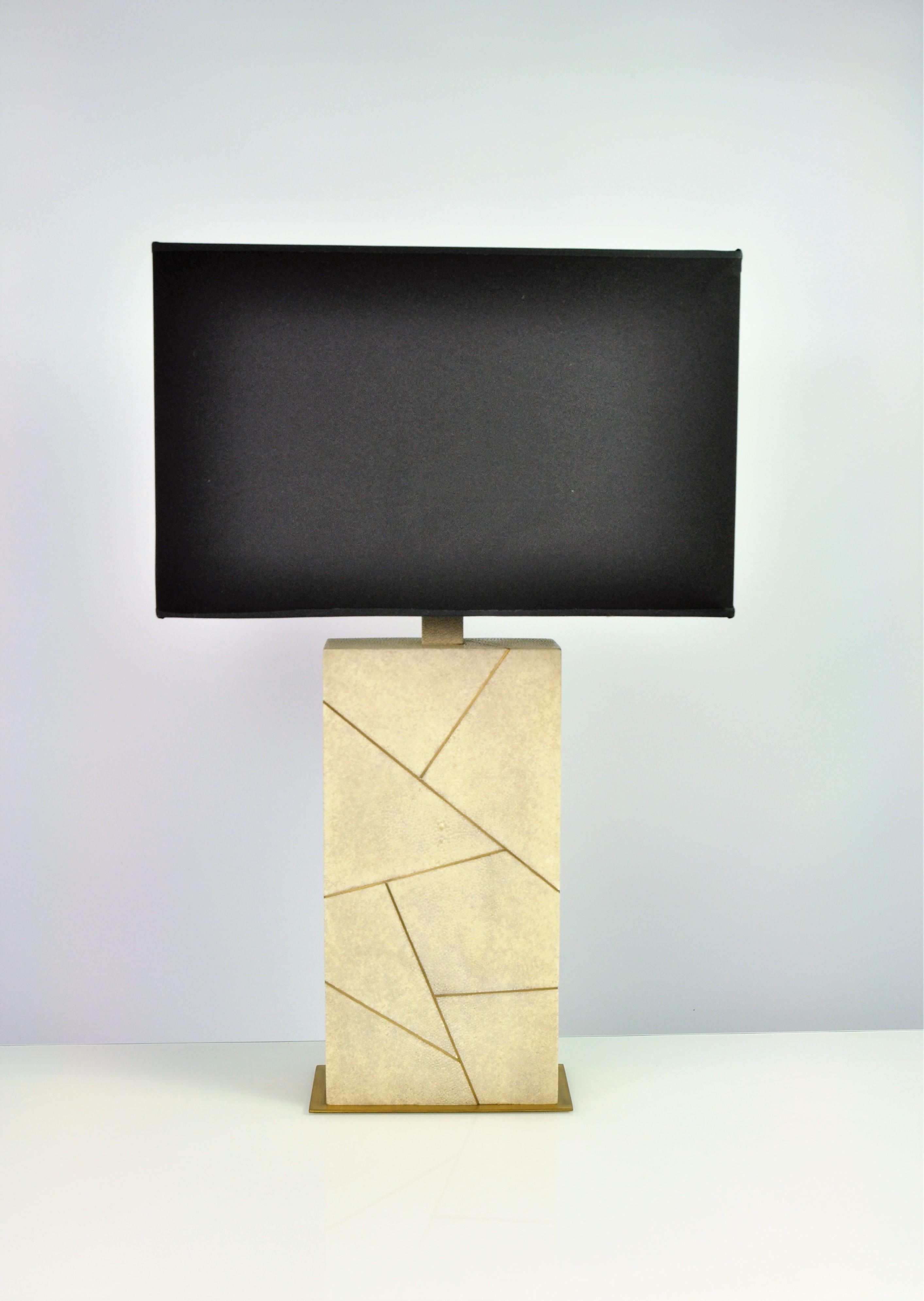 The table lamp CONSTELLATION by Ginger Brown is made of shagreen and brass trims.
The base is in brushed brass.
A revisited art-deco style. This piece will be nice in a classic or modern space. 

The shagreen is in natural color (Our ref
