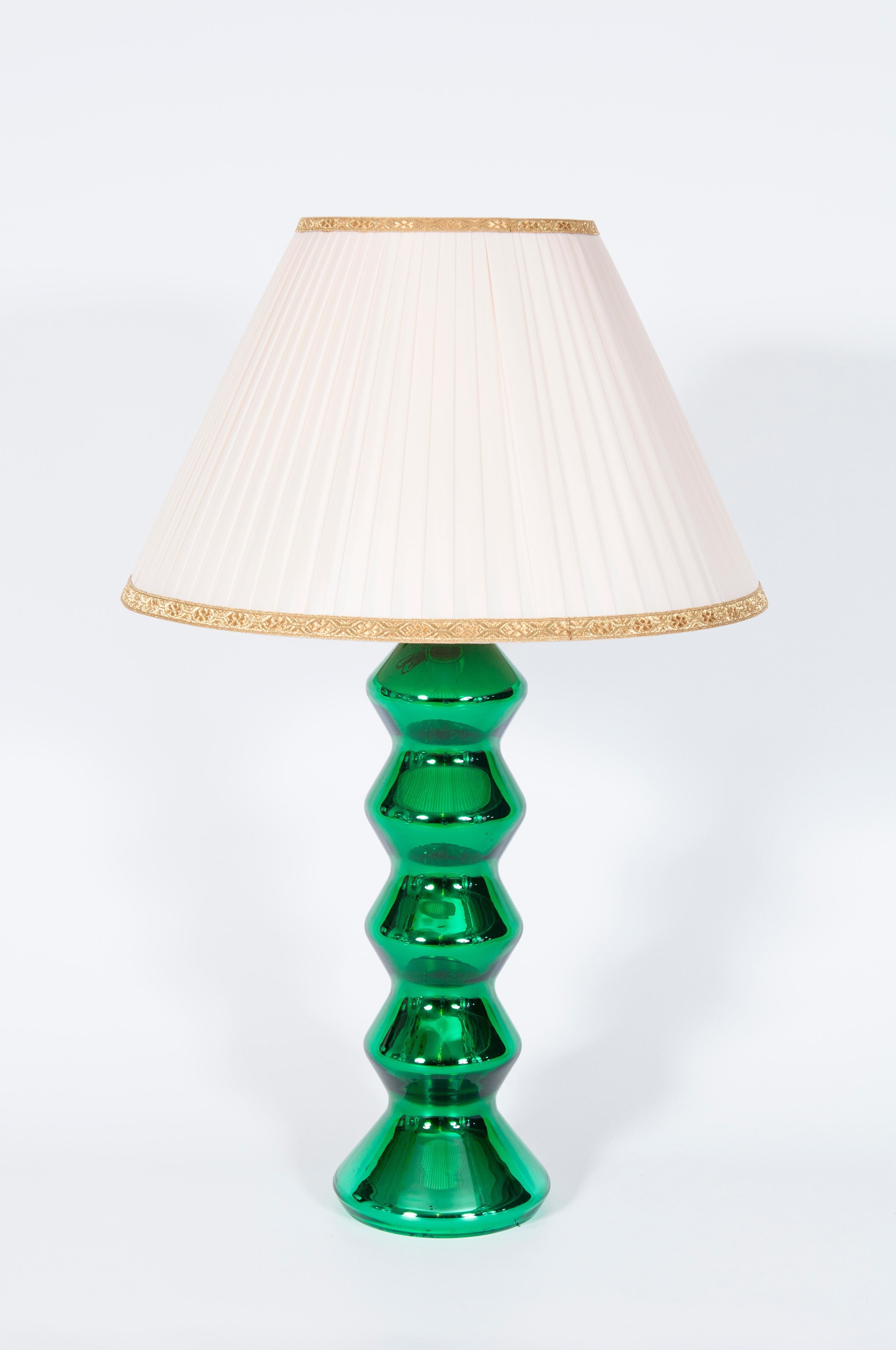This exquisite table lamp is a stunning example of 1970s Italian design, crafted from vibrant green mirror-colored Murano glass. The lamp's base features a striking sculptural form, with a series of stacked, undulating segments that create a dynamic