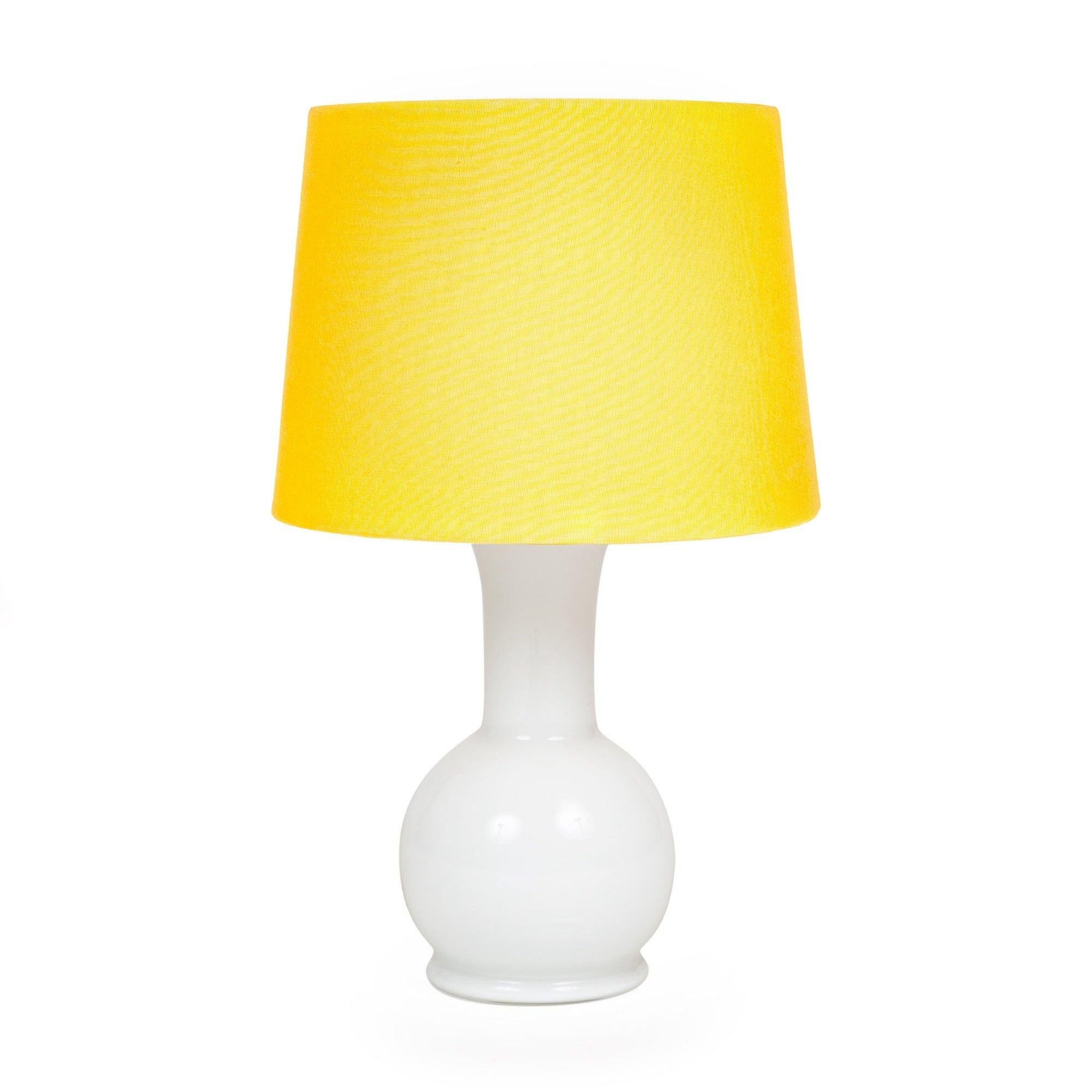 Lampe de table en verre bulbeux de petite taille en verre blanc opaque sous une partie supérieure en acrylique blanc qui sert à la fois de diffuseur pour la source lumineuse et de support pour l'abat-jour qui la dissimule.