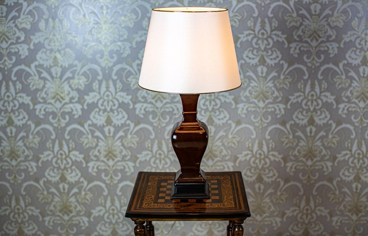We present you a table lamp from the 1980s with a ceramic base.
The lamp shade with a gold trim in the color of ecru is made of fabric (H: 26 cm).

There is a socket for a single E 27 light bulb.
The power source is 230 V.

This lamp is in