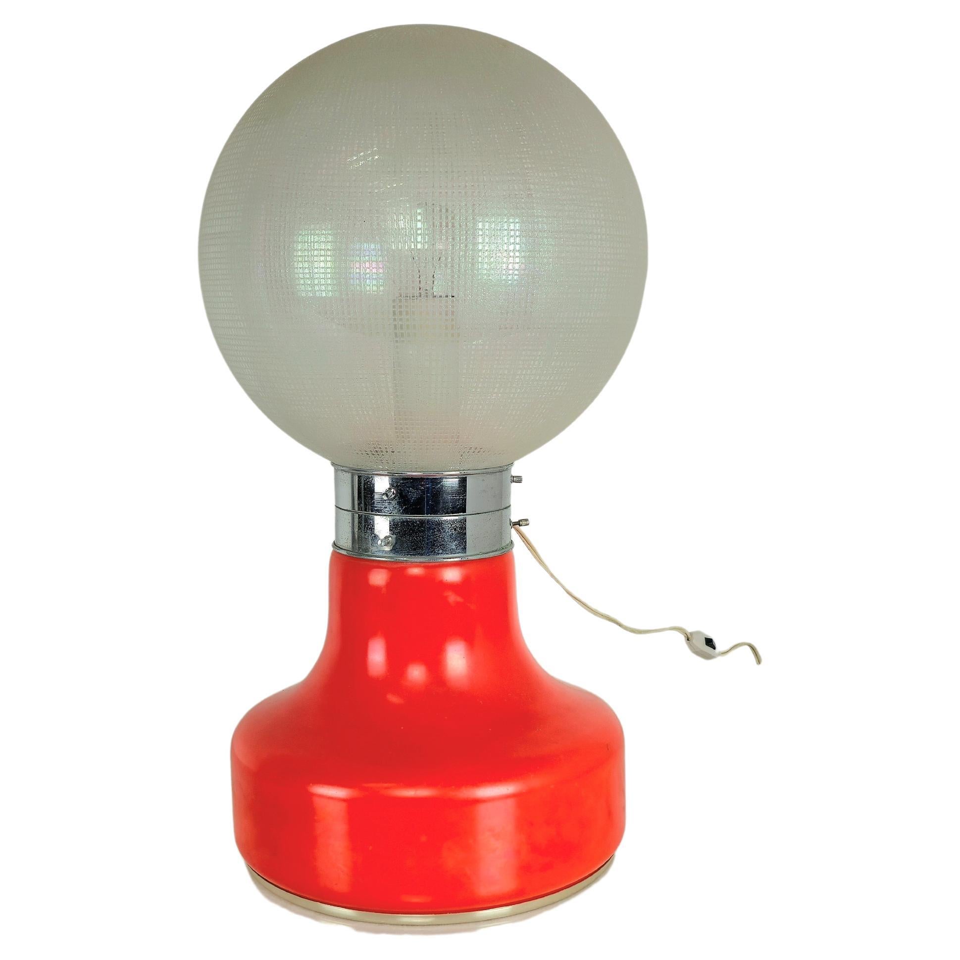 Lampe de table produite en Italie dans les années 60.
La lampe est composée d'un verre supérieur sphérique avec des carrés particuliers en relief sur toute sa surface et d'un verre inférieur dans des tons entre le rouge et l'orange. Les deux verres
