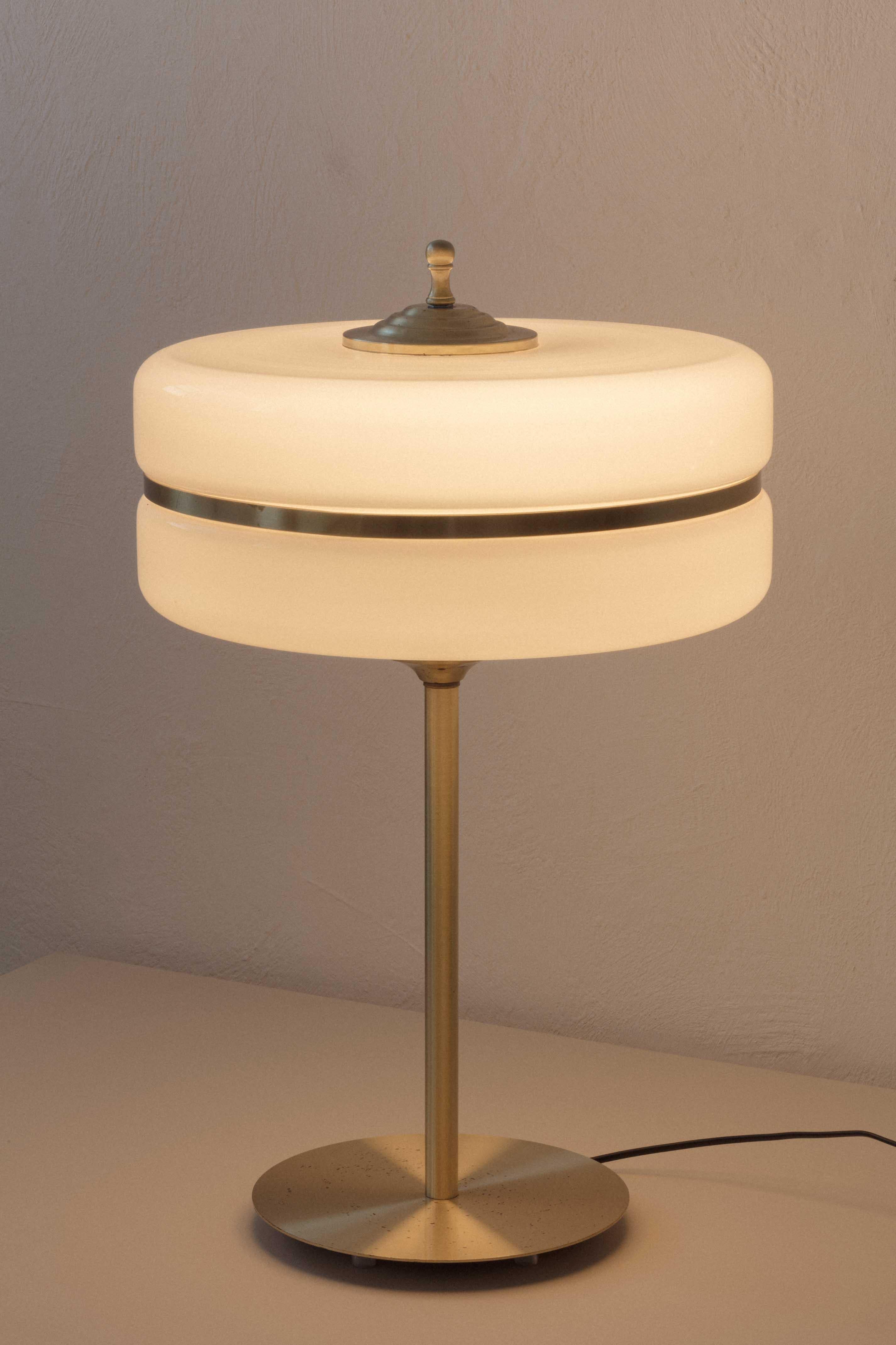 This gorgeous table lamp presents lampshades in glass, the most antique light diffusers. In this piece, the Deco-inspired opal cylindrical from the early 1900s tradition gains a simple and elegant design with brushed bronze structure and details.
