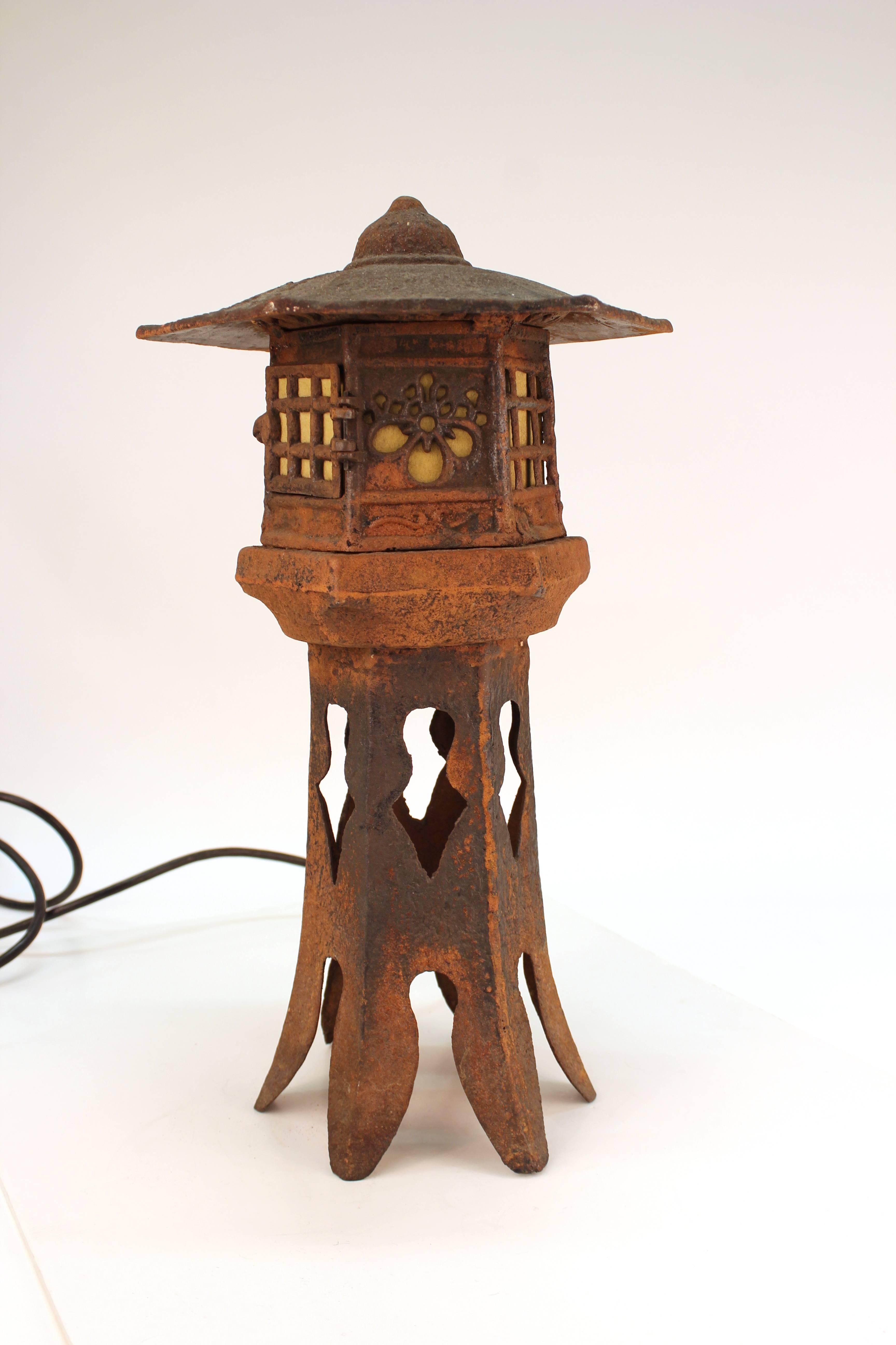 Table lamp crafted in cast iron in the form of a Pagoda. The piece stands on split petal legs while the bulbs are housed at the top of the tower behind screened 'windows.' The bulbs are accessible through a door at the head of the pagoda. The crown