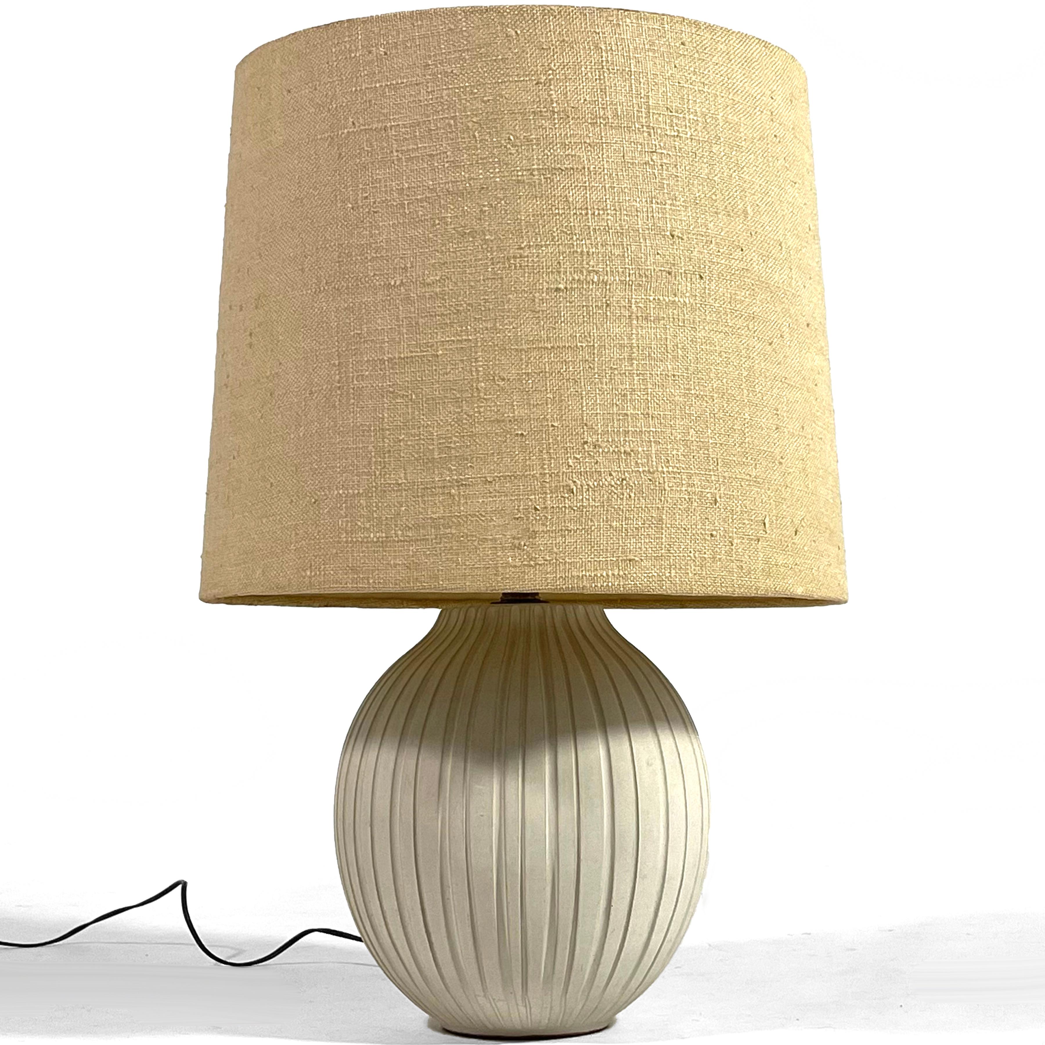 This exceptional table lamp has a hand made ceramic base in an onion shape with vertical incised lines. The original shade has a nubby linen texture, is perfectly proportioned and in very good original condition.