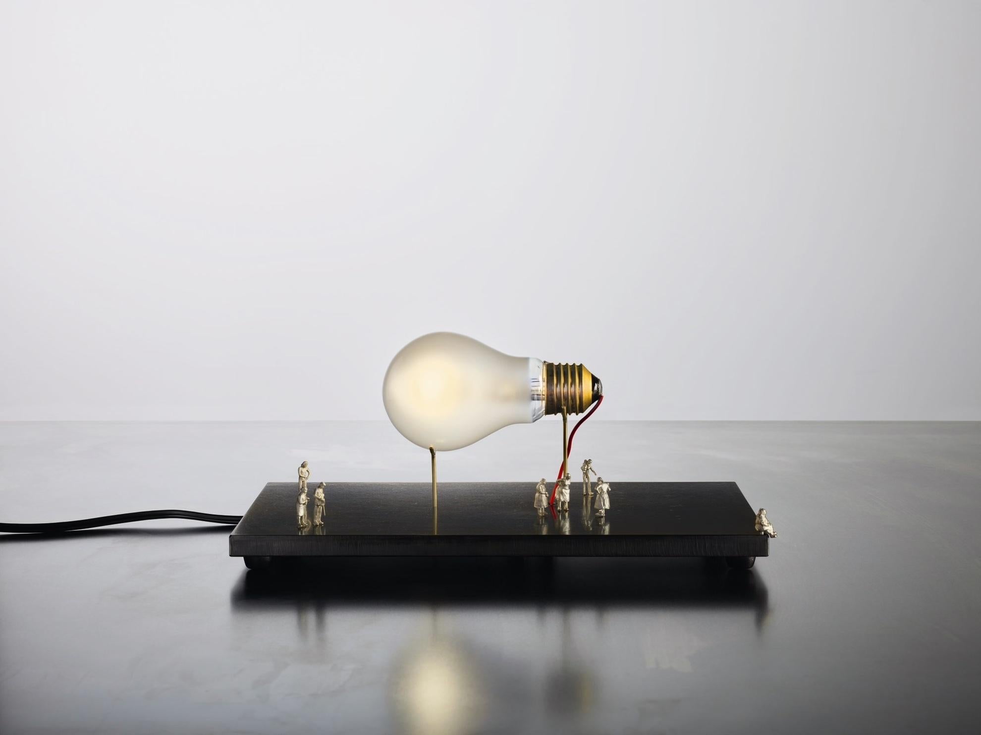I Ricchi Poveri – Monument for a Bulb
Designer: Ingo Maurer
Brand: Ingo Maurer

I Ricchi Poveri – Monument for a Bulb is a sculptural table lamp that transforms a single bulb into a miniature monument. Eight tiny figures, crafted from nickel silver,