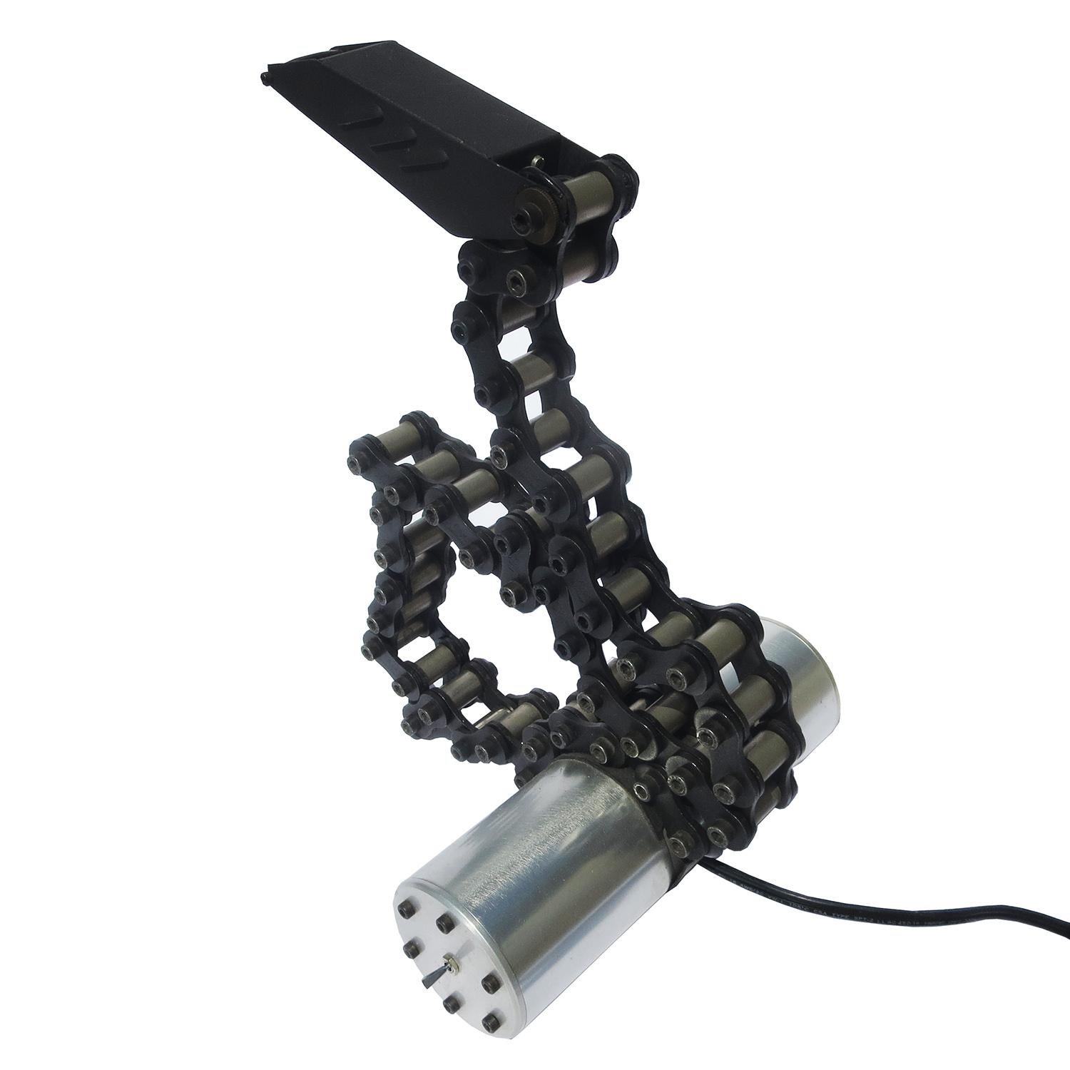 This unique lamp was created by an artist using a heavy duty motorcycle chain to conduct the electricity to the bulb. The cylindrical base houses a low voltage transformer to power the lamp. Although the chain links pas the low voltage to activate