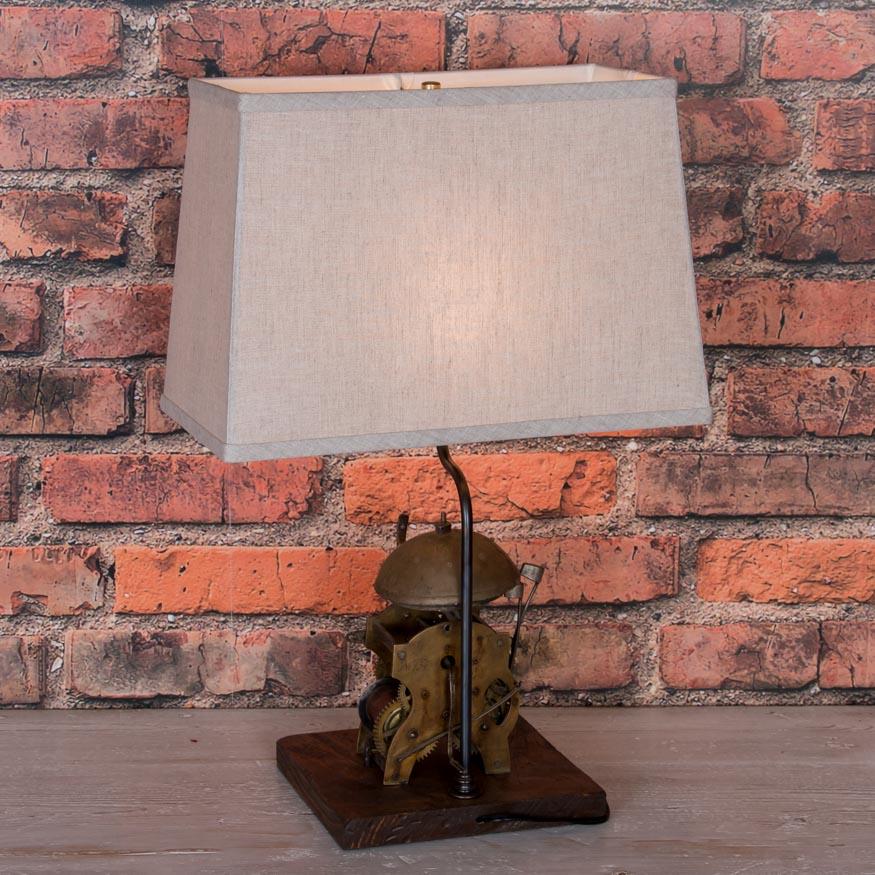 This unique table lamp has been made by re-purposing the original clockworks found inside a Swedish grandfather clock. The bell, striker and gears make for a fascinating lamp base, and it is balanced by the rectangular lamp shade on top. Please