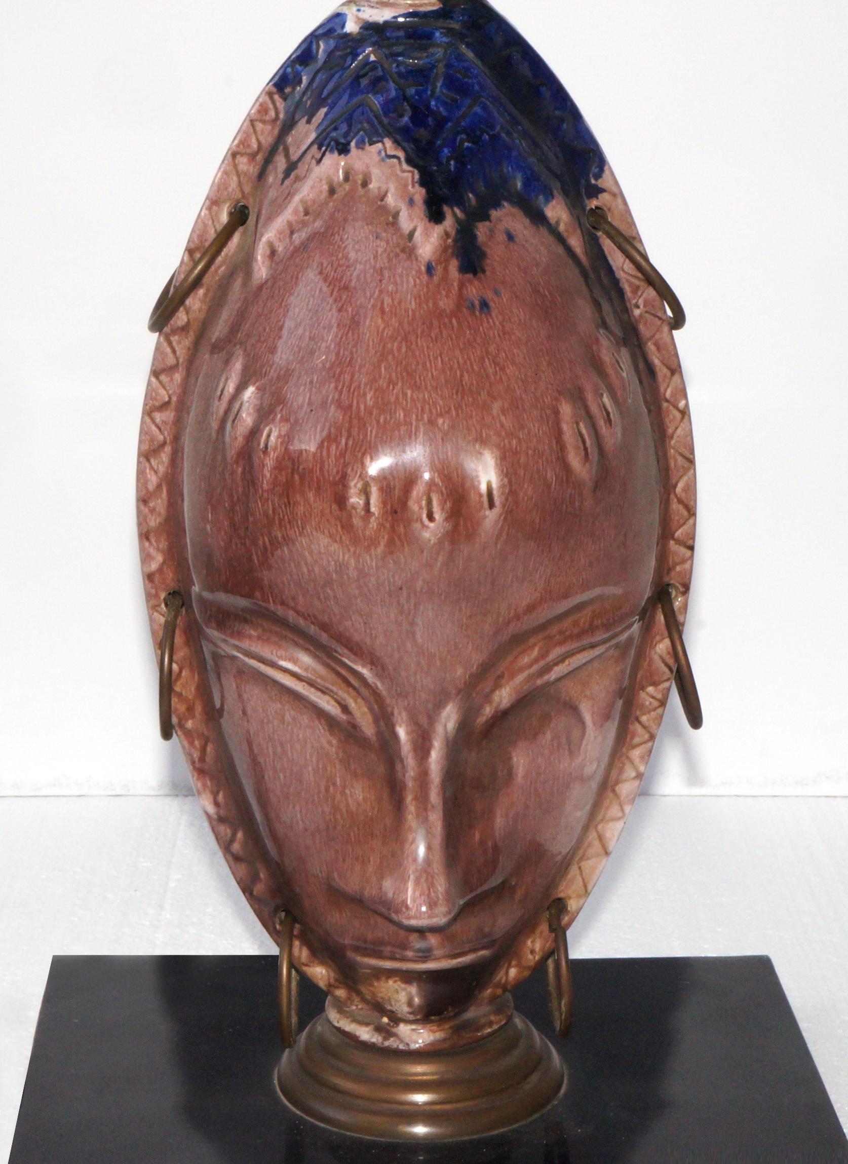 Lamp with the face of an African woman made in high temperature ceramics. They are two faces, one facing the front and one on the back creating an incredible optical illusion. Mounted on a lacquered iron base, with bronze details. Shade not included.