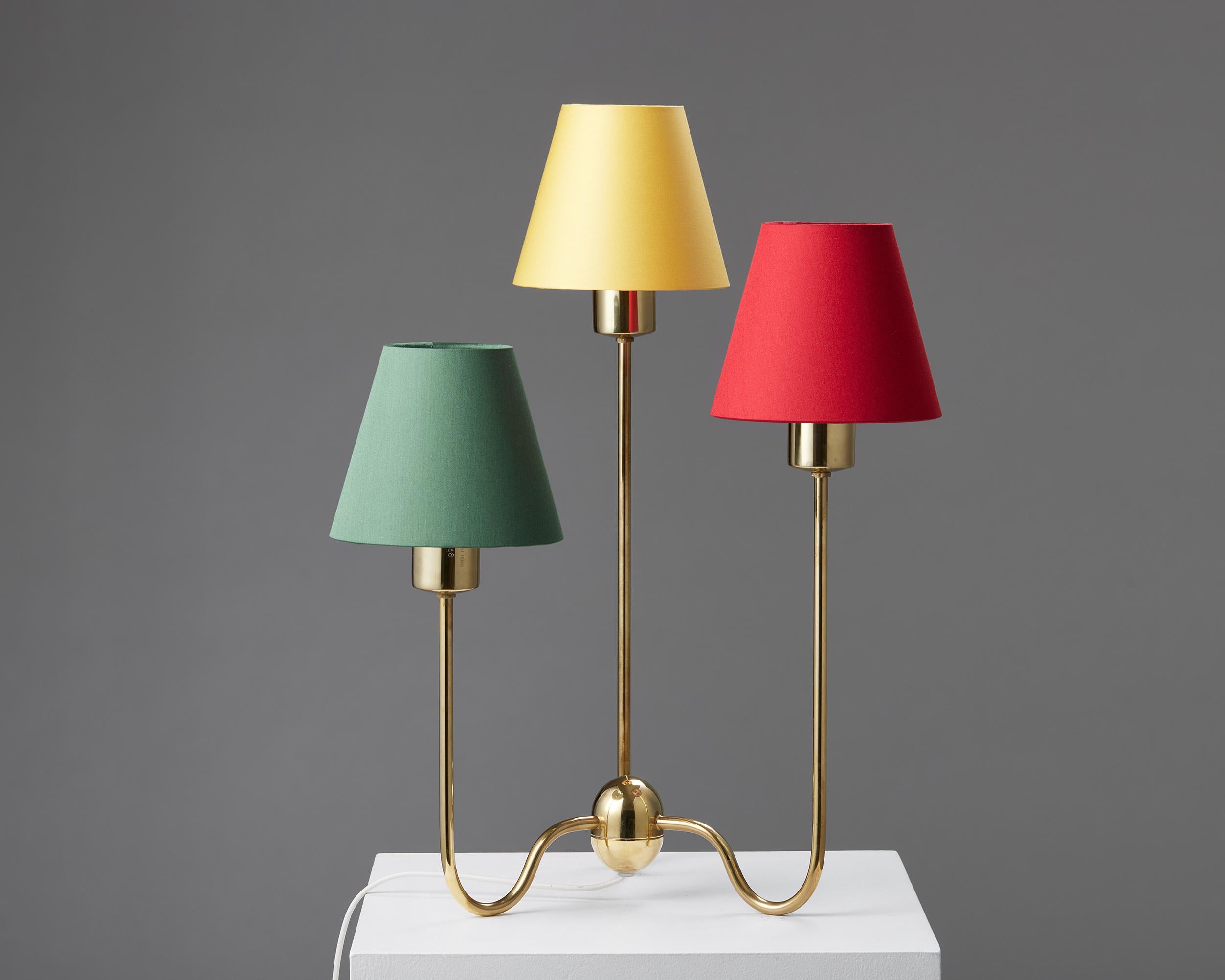 Brass with cotton shades.

Stamped.

Model 2468 is a delightful brass table lamp with three small shades in green, yellow, and red. The lamp has an elegant brass base with three stems that hold the shades at different heights. Because of its