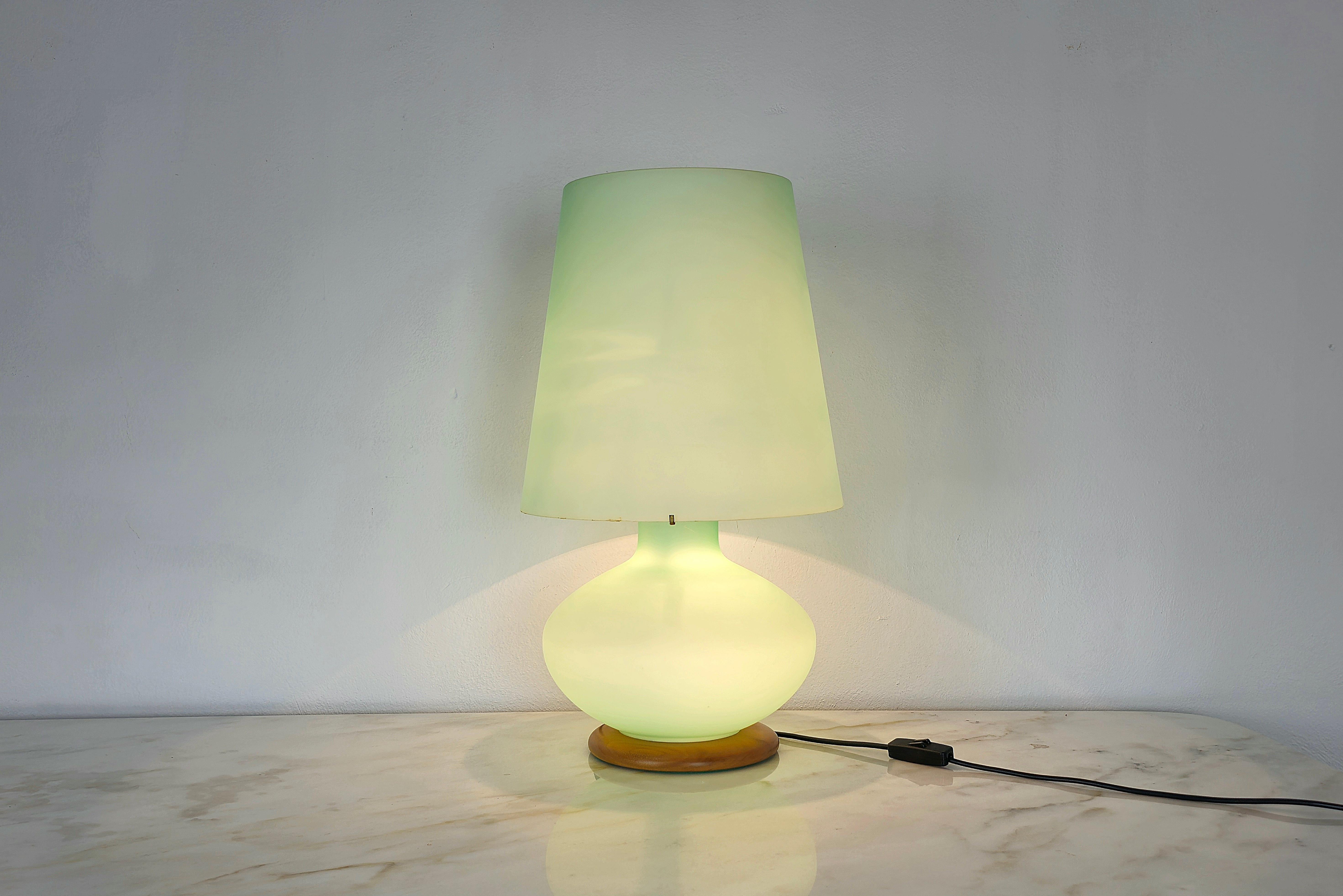 Large table lamp made of hand-worked layered Murano glass in aqua green color with a circular wooden base and metal accessories. The management of the light can be managed thanks to the switch, alternating the lights to your liking. Made in Murano