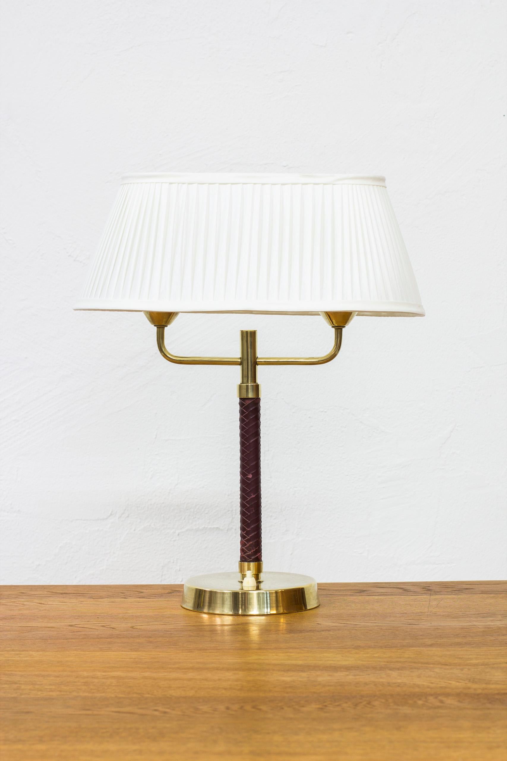 Table lamp produced by Karlskrona lampfabrik in Sweden. Made sometime between the 1940s-1950s. Made from solid brass with original leather on the stem. Original lamp shade with new pleated hand sewn chintz fabric. Light switch on the base in working