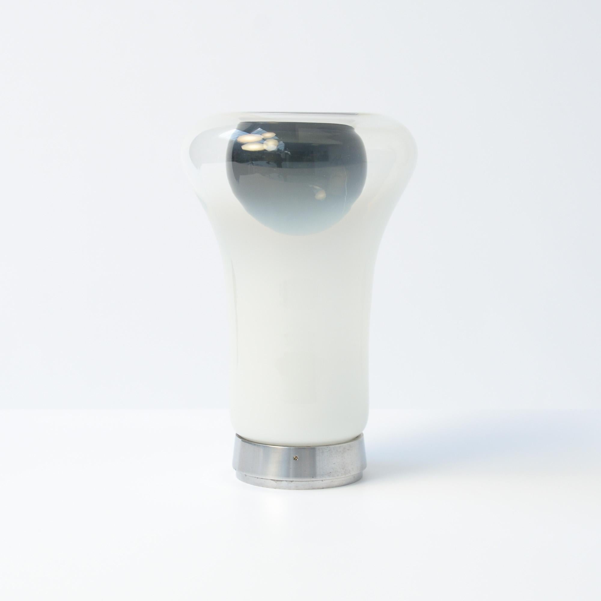The Saffo table lamp was designed by Angelo Mangiarotti for Artemide in 1967. It was named after the Greek lyric poet Sappho.
The aluminum base supports the mushroom shade in blown smoked Murano glass. The glass is mouth blown in two colors and in