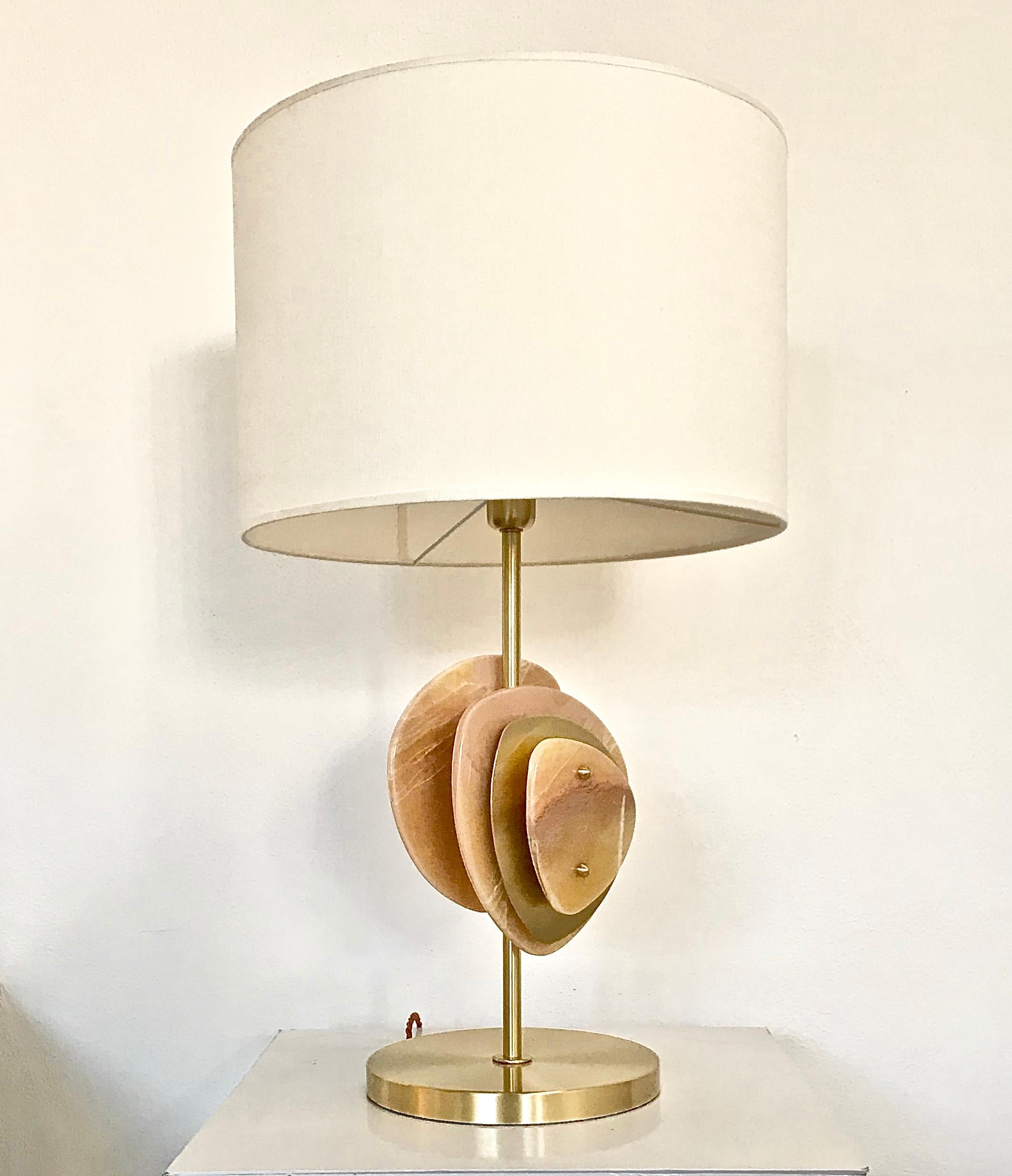 Table lamp base in satin brass with double 3-layer decorative elements on the stem in polished honey onyx and satin brass. 1 lightbulb holder E27 and braided twisted 3-pole electric cable. Cylindrical lampshade in ivory linen.