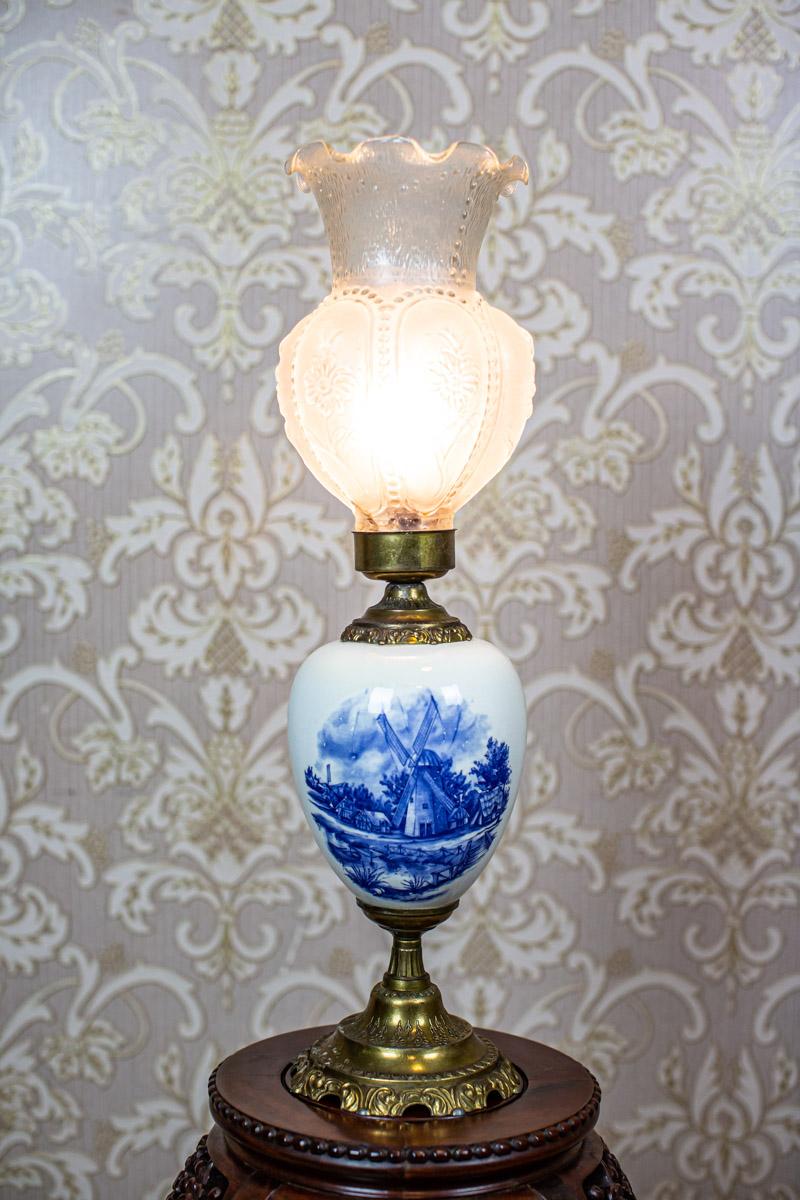 Brass and Faïence Table Lamp Stylized as Kerosene Lamp, circa the 1980s/1990s

We present you a modern electric lamp, whose shape is based on a kerosene lamp.
The base is made of brass combined with faïence from Delft, whereas the shade is of milk