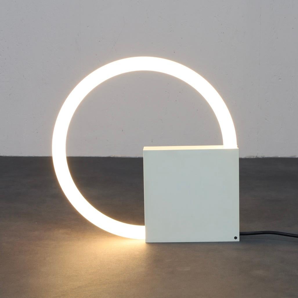 This iconic TC6 lamp, designed by Aldo van Nieuwelaar in the 1970s for Artimeta, is a striking example of minimalist lighting design. It features a bold geometric composition: a perfectly circular light ring intersecting with a crisp, white cubic