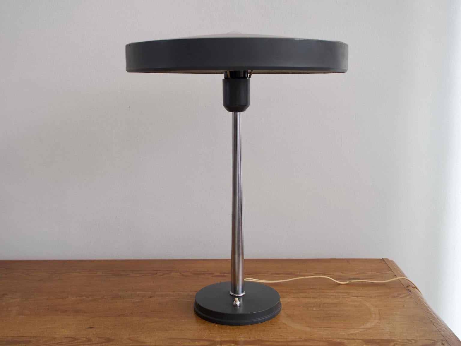 Model Timor desk lamp was designed by Louis Kalff for Philips and it is one of his most famous designs. The lamps features a conically shaped chromed steel rod and dark grey painted aluminum base and round screen. European plug.