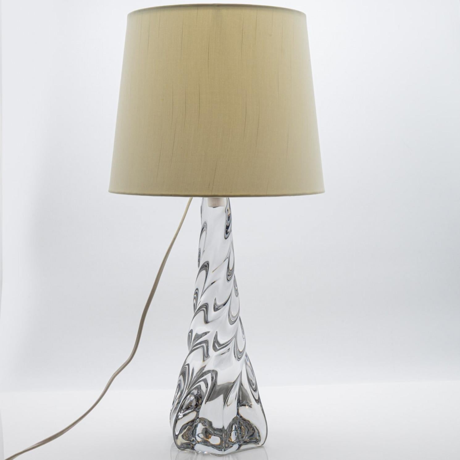 Esta elegante lámpara de sobremesa presenta una escultural base de cristal con un diseño fluido y retorcido que capta y refleja maravillosamente la luz. La forma de cristal transparente le da una sensación de movimiento y sofisticación, que la hace