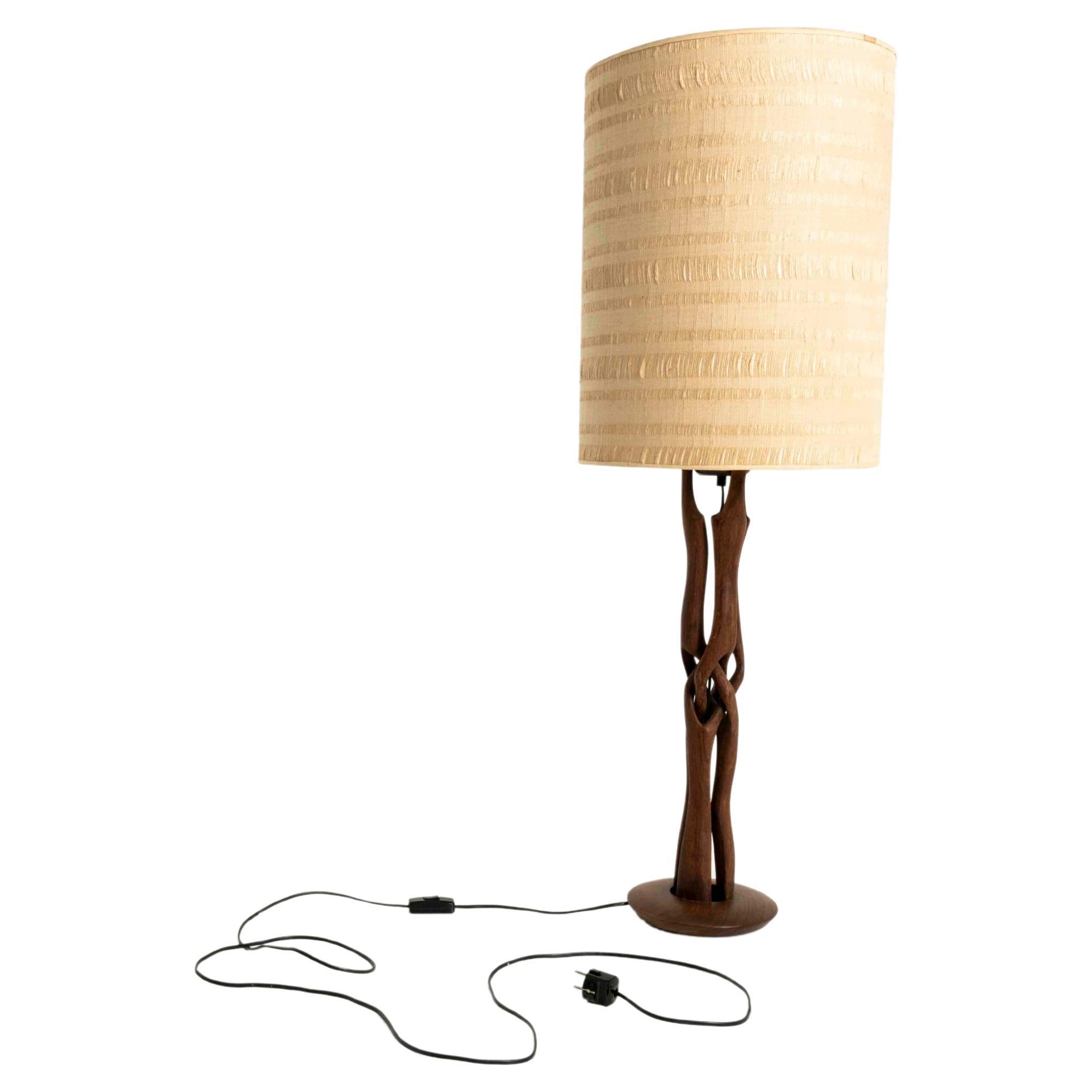 Beautiful table lamp with an abstract carved, wooden base. The lamp has an off-white lamp hood, which gives it a very nice contrast with the warm wood of the base. The lamp is in good condition with some small wear and tear on the hood of the lamp.