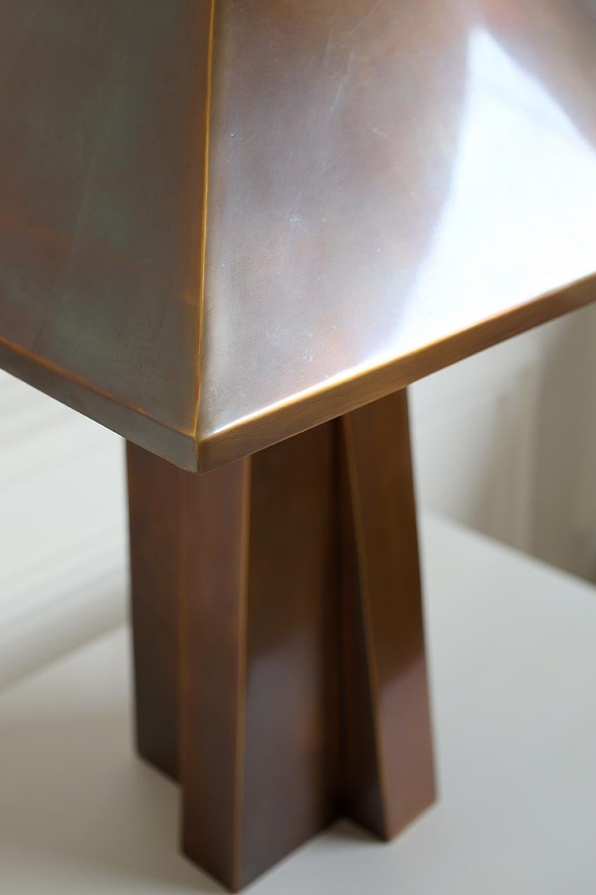 Antique brass table lamp with a pyramidal-shaped metal shade resting atop a thick sculptural base, giving the lamp a modern industrial aesthetic.
Handcrafted product. 
Surface finish and colour will vary in each piece. 
Colour cannot be truly