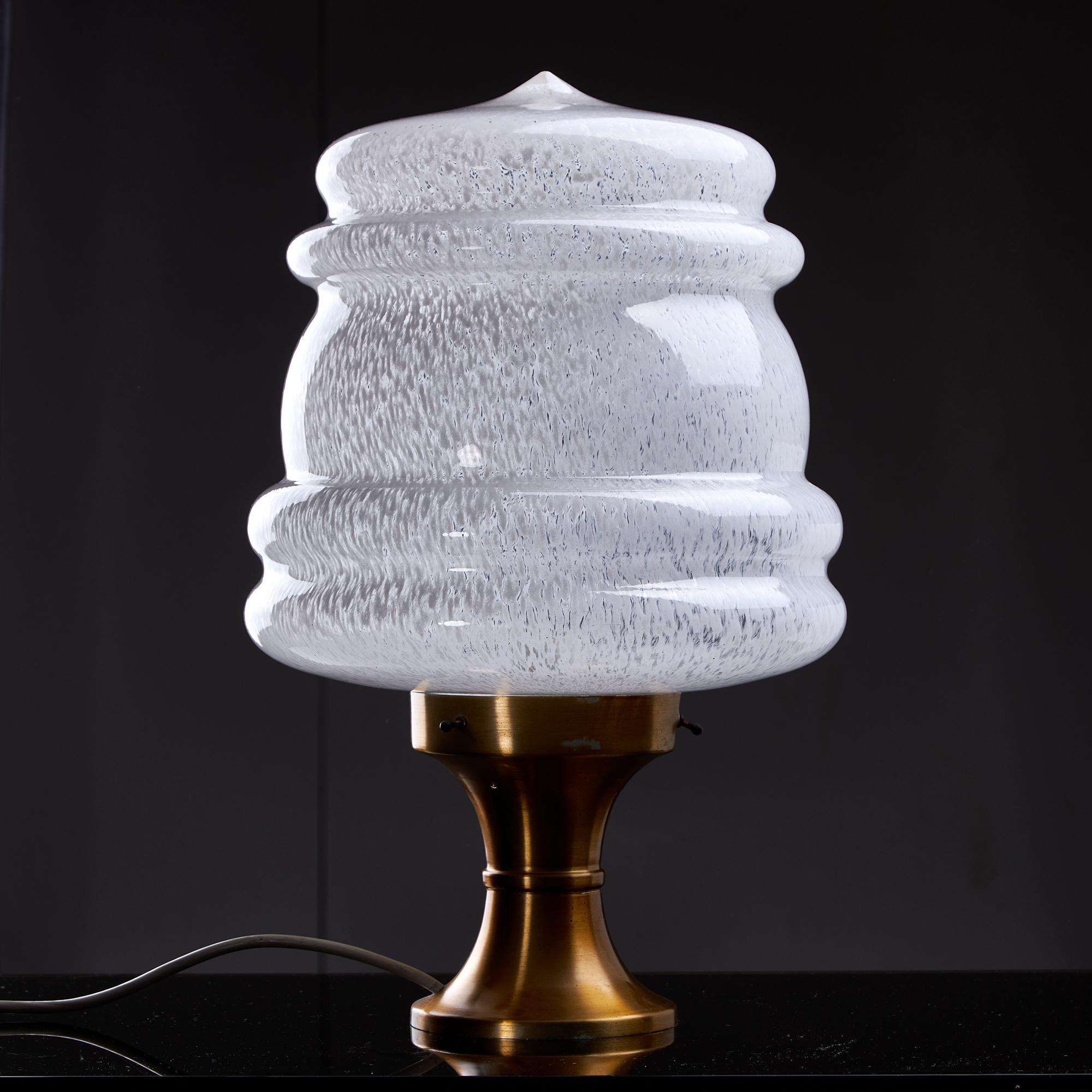 Esta lámpara de sobremesa tiene una base de latón que realmente destaca, y sostiene una delicada pantalla de cristal de Murano decorada con lunares blancos. La pantalla de la lámpara tiene una forma intrigante, que recuerda a las olas, pero también
