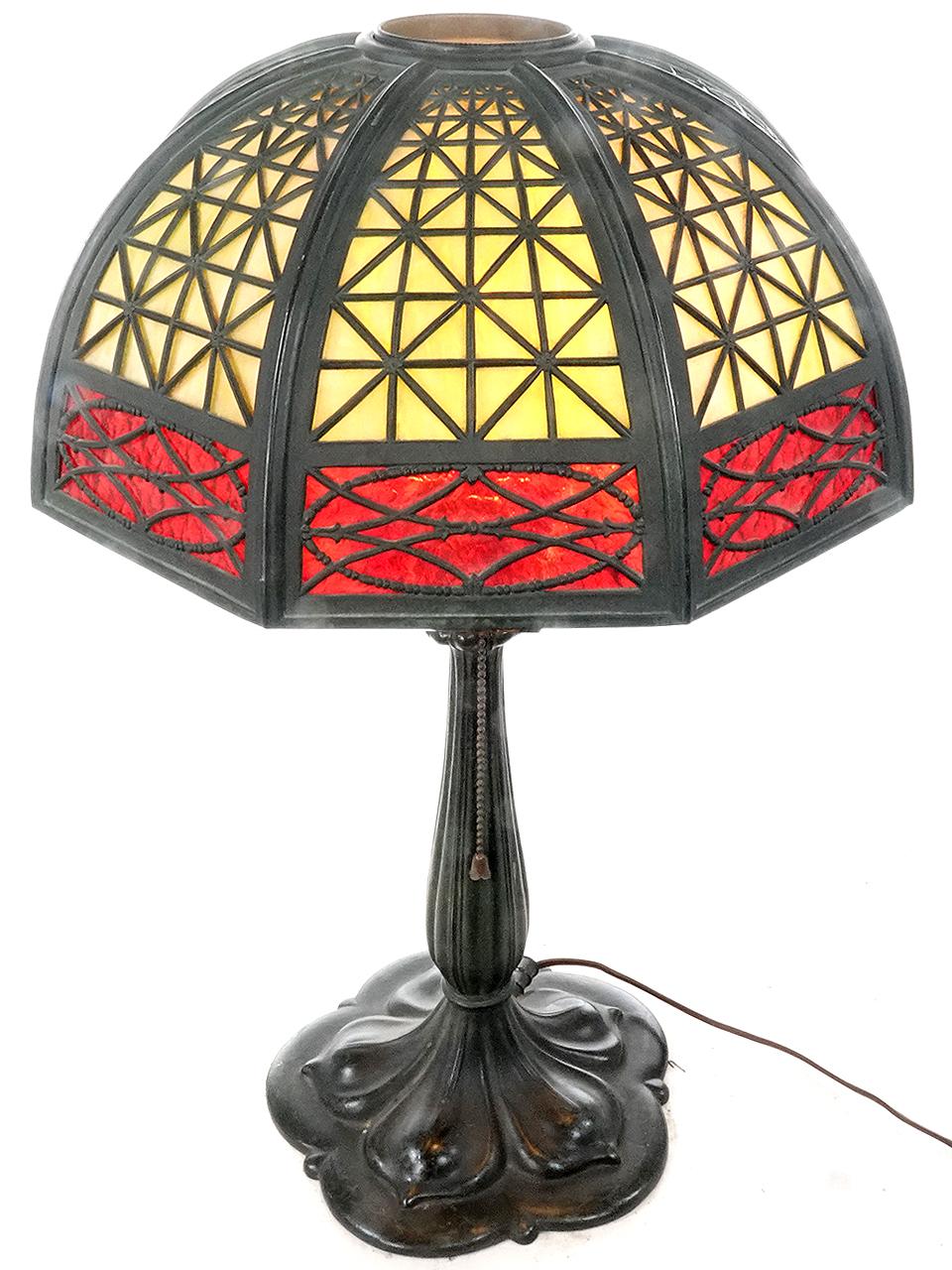 This is a nicely designed Arts and Crafts table lamp. It has a curved shade with 12 unique patterned latticework filigree overlays. Highly detailed but still simple and elegant. Each slump glass (curved) panel features a yellow amber variegated