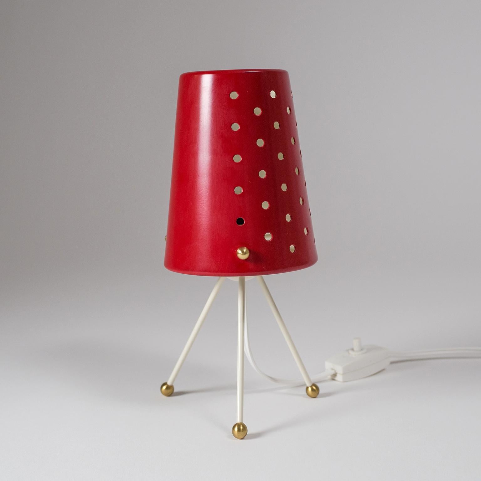 Delightful small midcentury tripod table lamp with a red lacquered shade and brass details. The shade is pierced on one half while the other half is solid. This allows for different light settings and when using a clear bulb creates a charming light