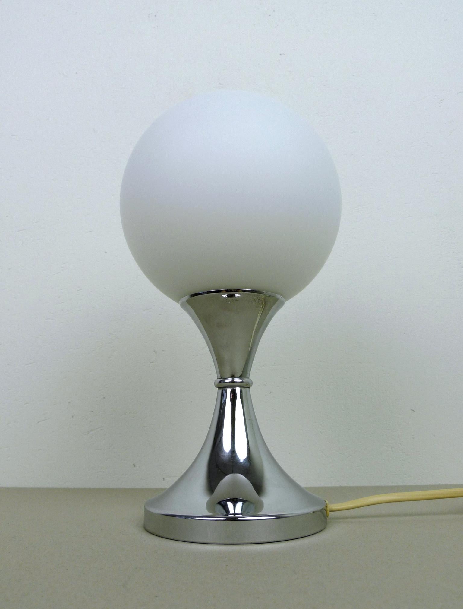 This vintage table lamp features a white opal glass shade and a trumpet-shaped stand in chromed metal. Inside there is an E 14 bulb socket. 
The lamp was produced in Germany in the 1960s and it is in good condition.