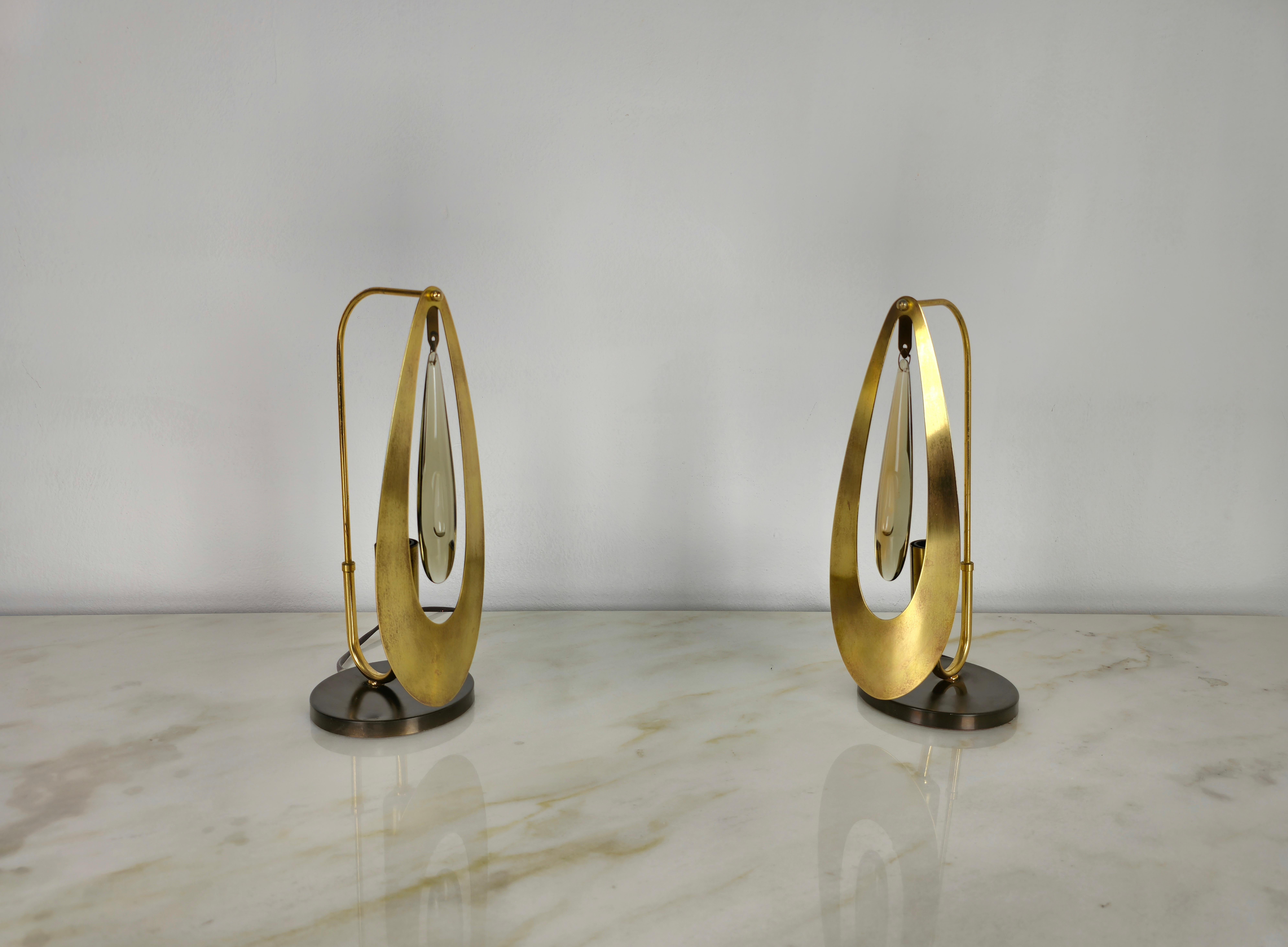 Rare et élégante paire de lampes de table fabriquées en Italie dans les années 1960/70.
Chaque lampe est composée d'une base circulaire en laiton bronzé, d'une structure métallique dorée incurvée, d'un pendentif en verre de cristal et d'une grande