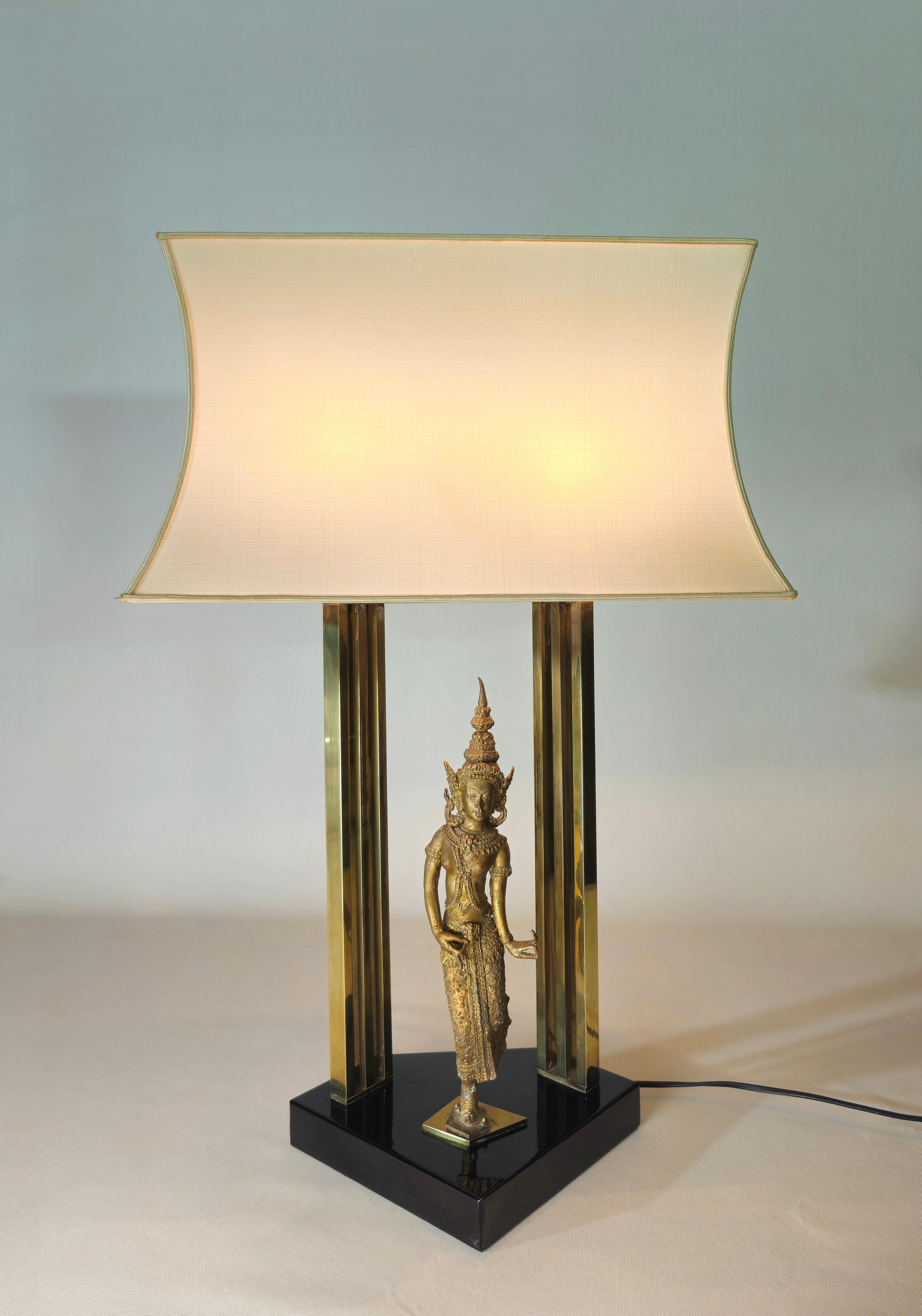 Table lamp of considerable dimensions produced in Italy in the 60/70s. Brass structure, black enamelled base and fabric diffuser. In the center there is a sculpture depicting a dancer from the Thai temple in gilded and chiseled bronze. Unfortunately