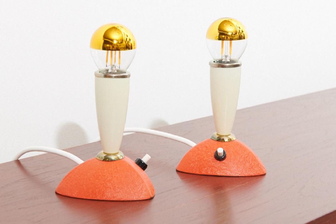 Restored: table lamps / debside lamps Duo Rubo, 1957 , bakelite cone sockets in light gray with gold ring, metal feet with coral red shrink lacquer, push-button, 2x E14

Height: 12cm
Diameter: 11.5cm.