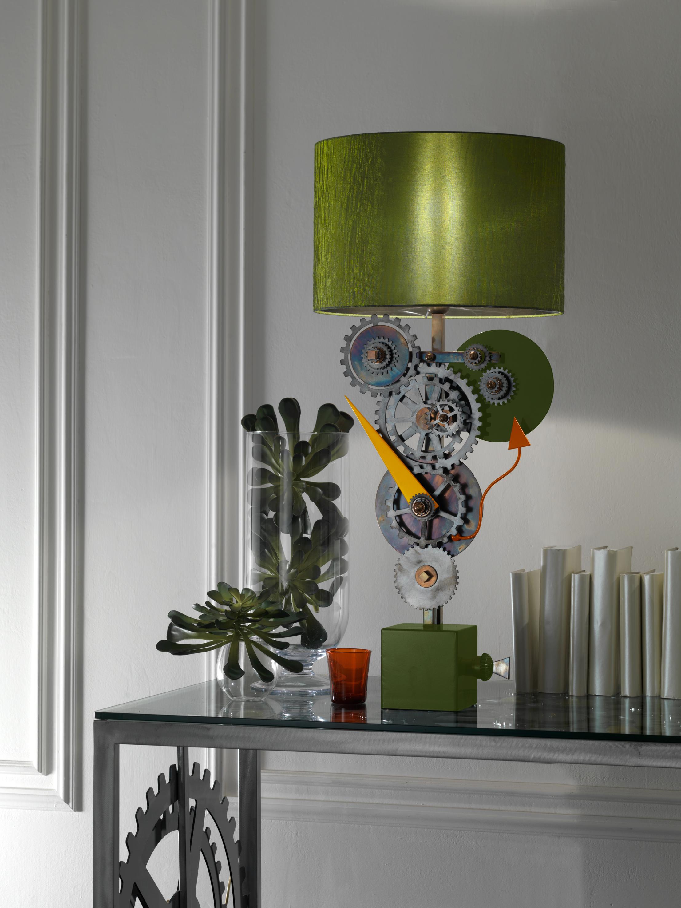 Burnished brass wall lamp with iron gear wheels in pewter finish. Green base, orange and yellow minute hands, burnished brass and green details. Green silk lampshade.