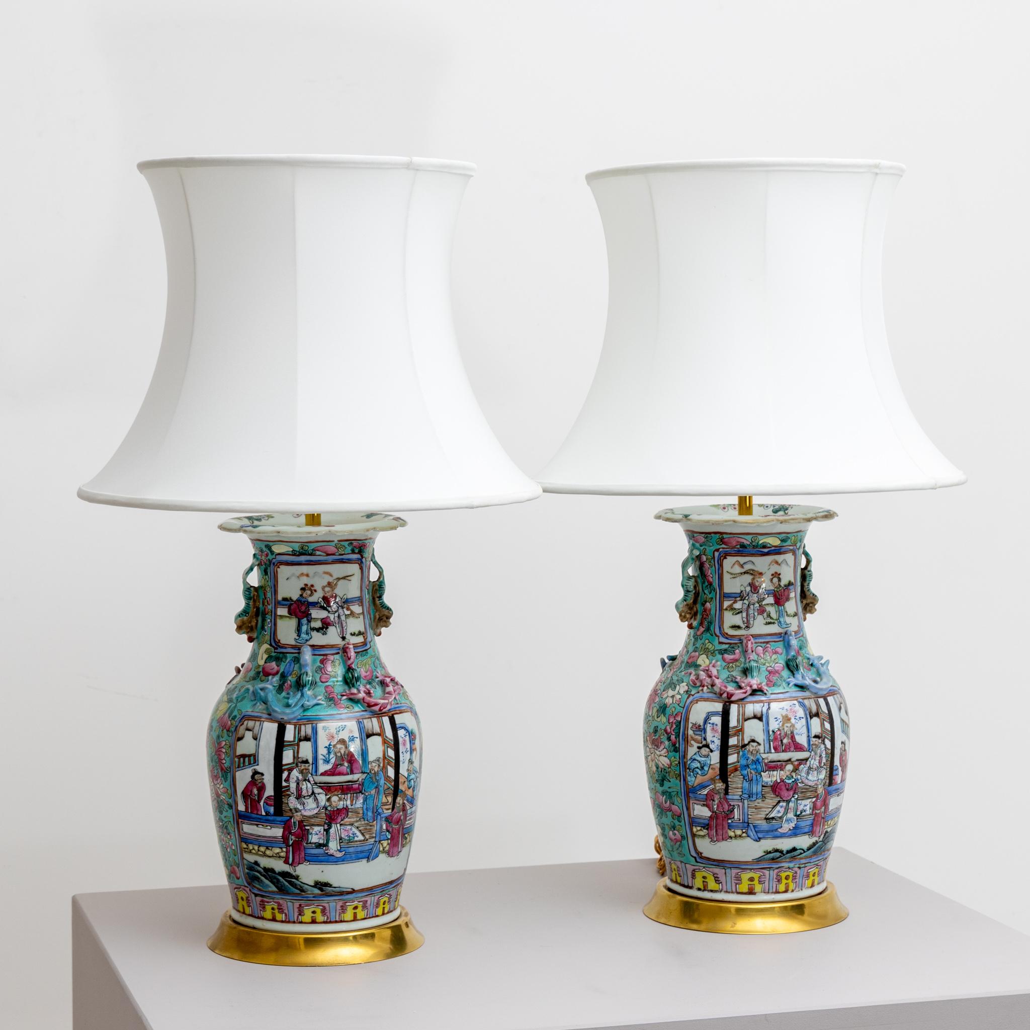 Pair of table lamps with polychrome painted porcelain vases as lamp bases and white fabric shades. One Lamp with old repairs.