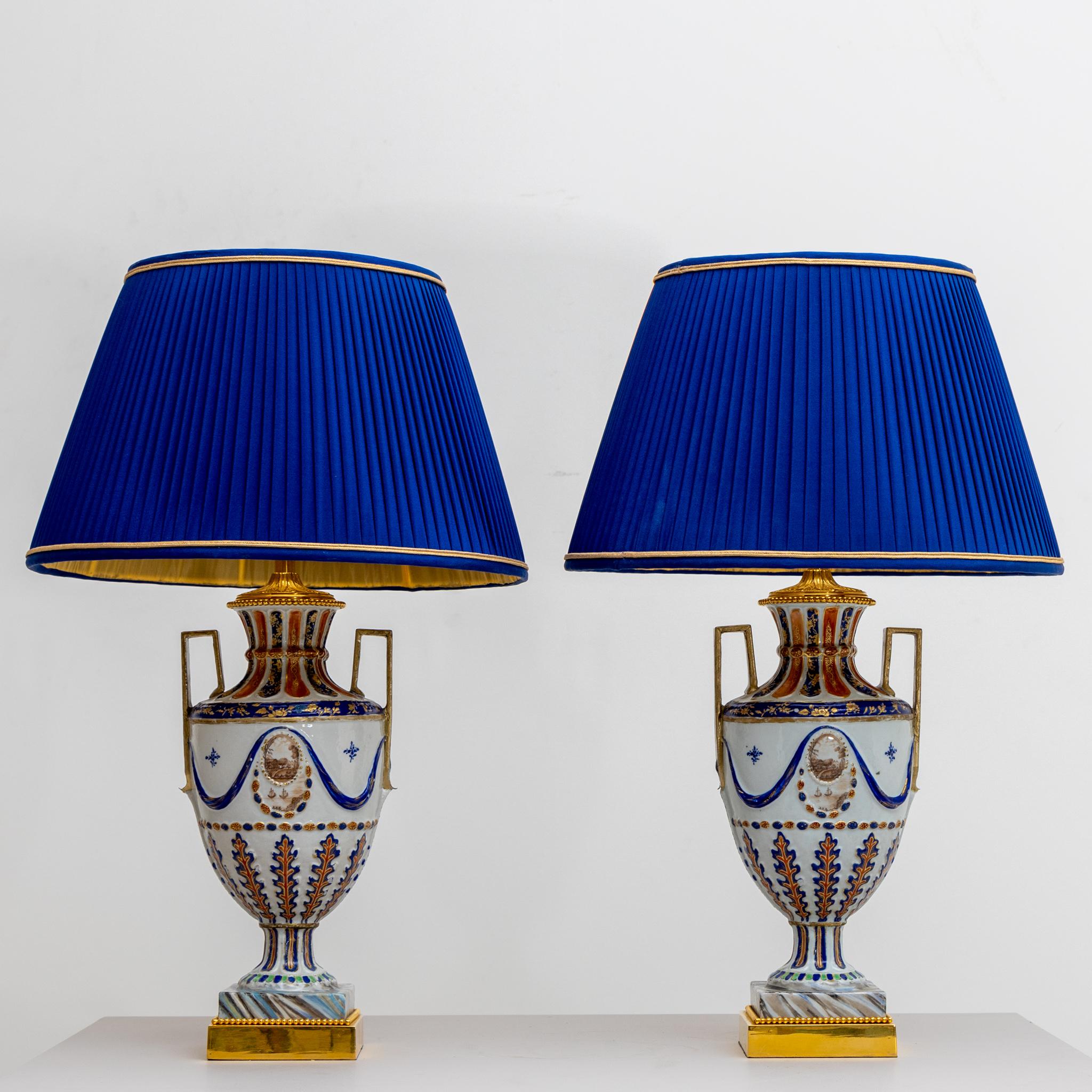 Pair of table lamps with amphora shaped polychrome painted porcelain lamp bases and blue fabric lampshades.