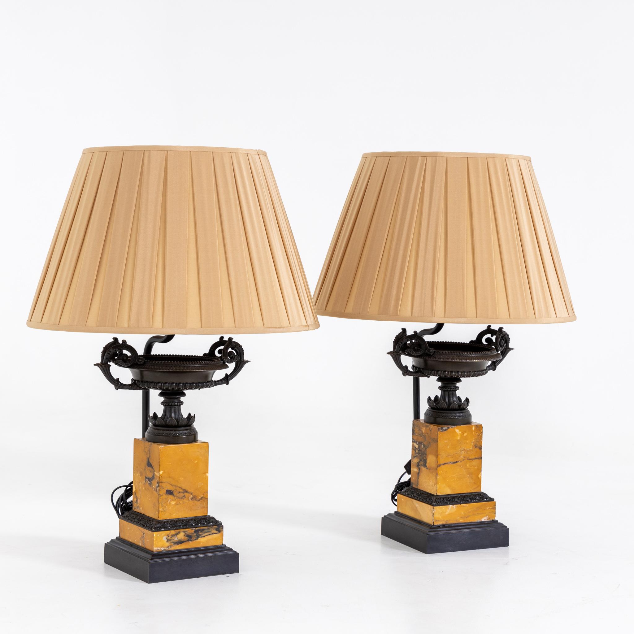 Pair of lamps with tazza over square pedestals of yellow marble and black plinths.