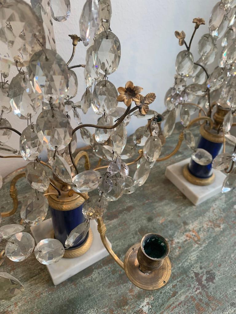 Gustavian table lusters, made in Stockholm from about 1800. A pair of beautiful table lusters in gilded brass. The top is decorated with a cresent moon. In the center there is a blue glas obelisk. The foot is made of white marble from Carrara. The
