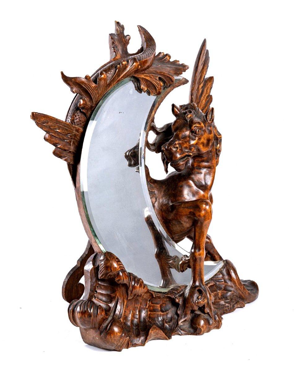 A delightful table mirror in the shape of a bevelled crescent moon, around which a magnificent wooden sculpture, with rounded and muscular forms, is wrapped, representing Pegasus, with his wings spread, defender and protector of this beautiful moon,