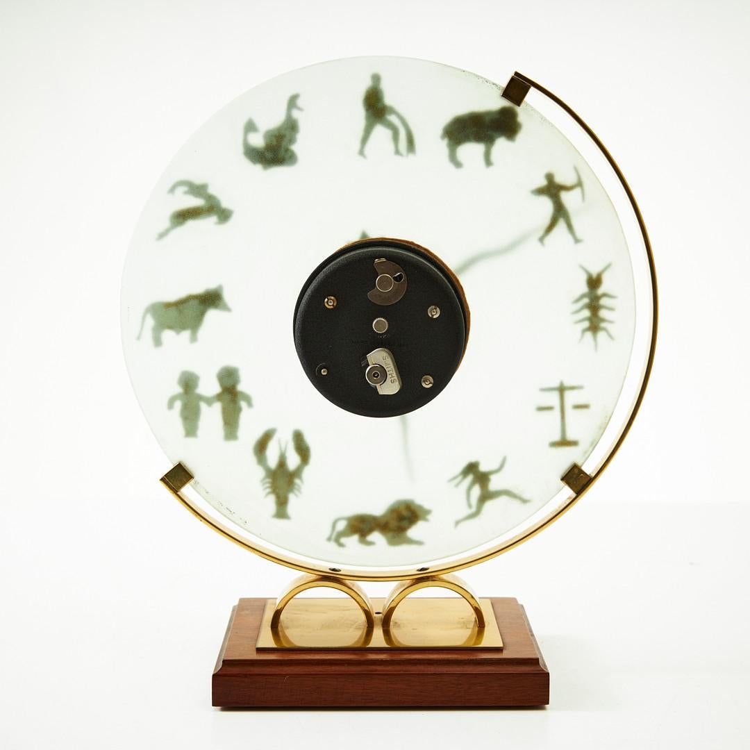 Midcentury table clock, brass frame with glass clock face with zodiac motifes on hardwood base. Made in UK in the 1950s by Smiths English Clock Systems. 
