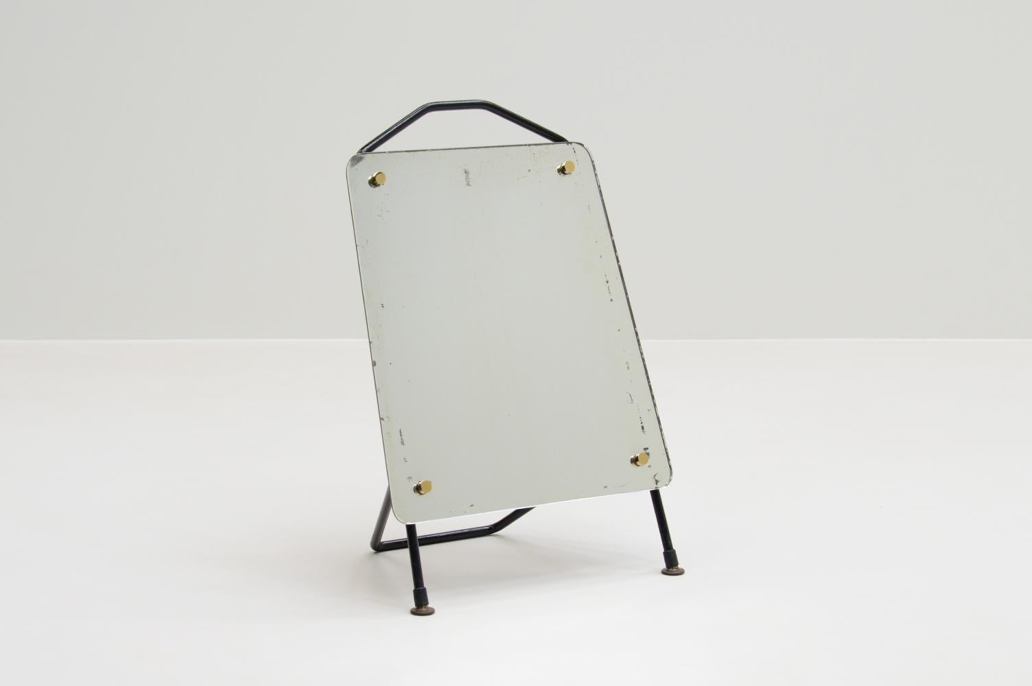 Table or shoe mirror, France 1960s. Black metal frame, tapered shape mirror and brass details. Because of the angle it can be used as a table or shoe mirror. The mirror has a nice patina. In good vintage condition. 


