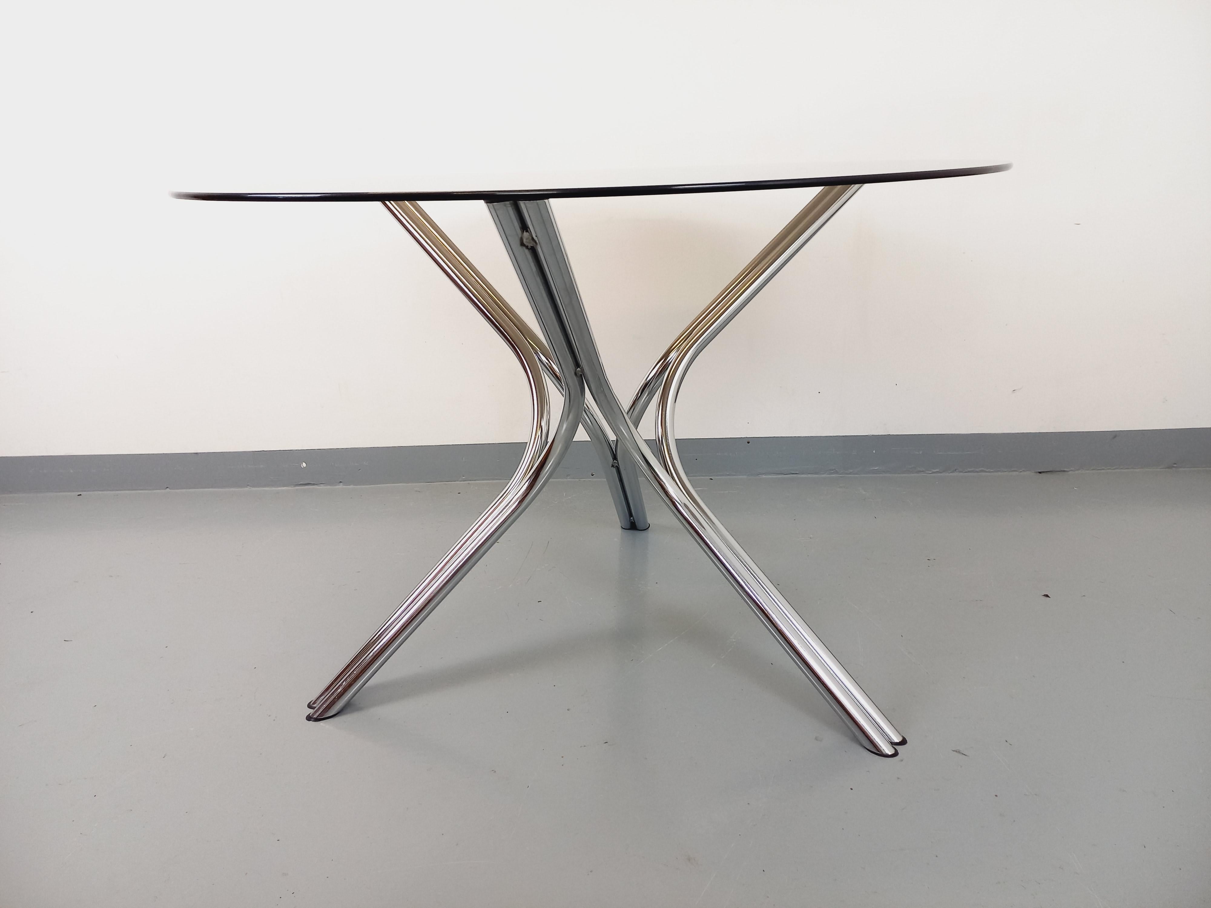 Table ronde à manger vintage des années 70, style Space AGE, plateau rond en verre fumé, pied en métal chromé en X design et original, très bon état, chrome en très bon état, plateau en très bon état avec seulement quelques très rares micro-rayures