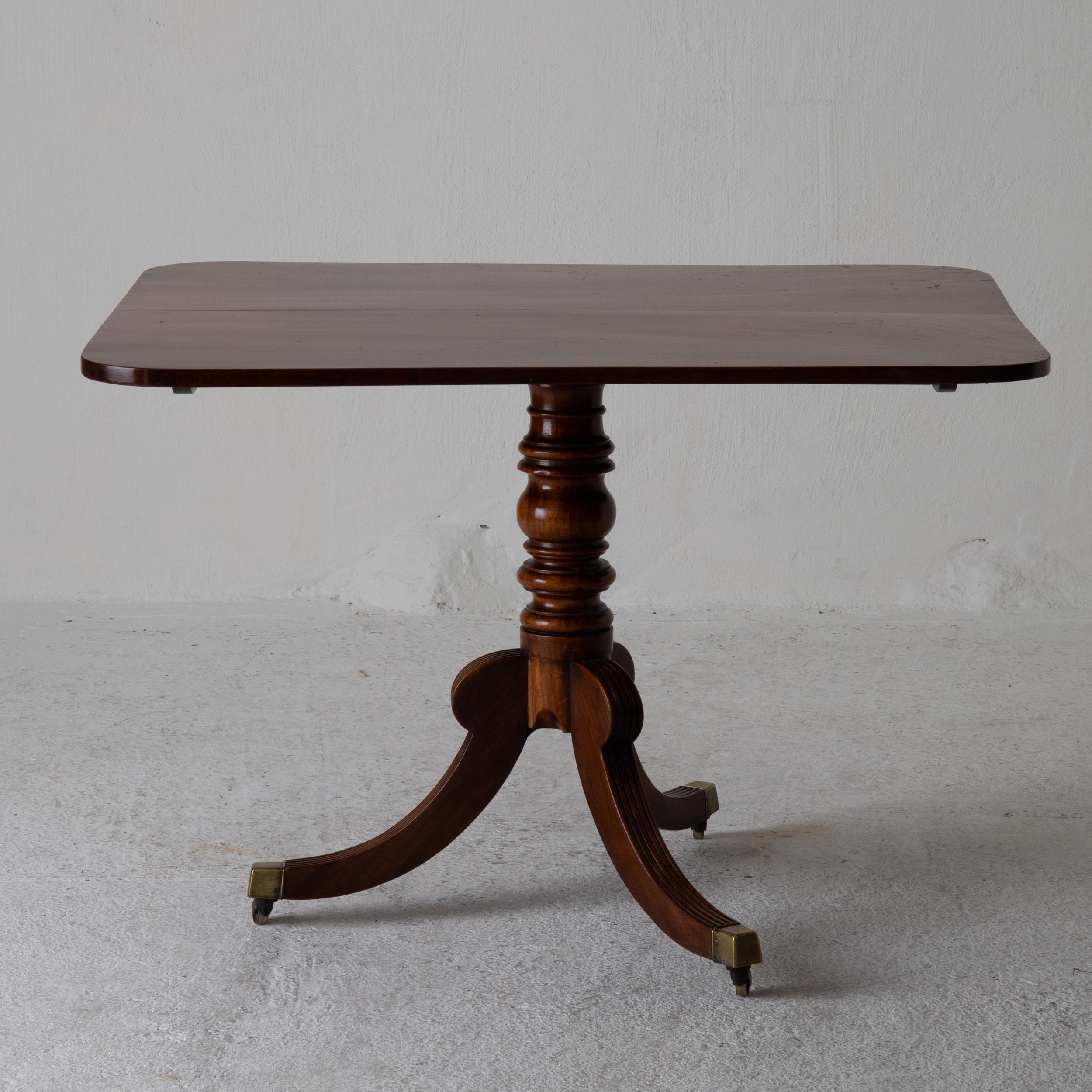Table tilt-top English mahogany, 18th century. A table made during the Victorian period in England. Dark brown mahogany. Rectangular top with rounded corners. Tripod base ending in brass casters with wheels.