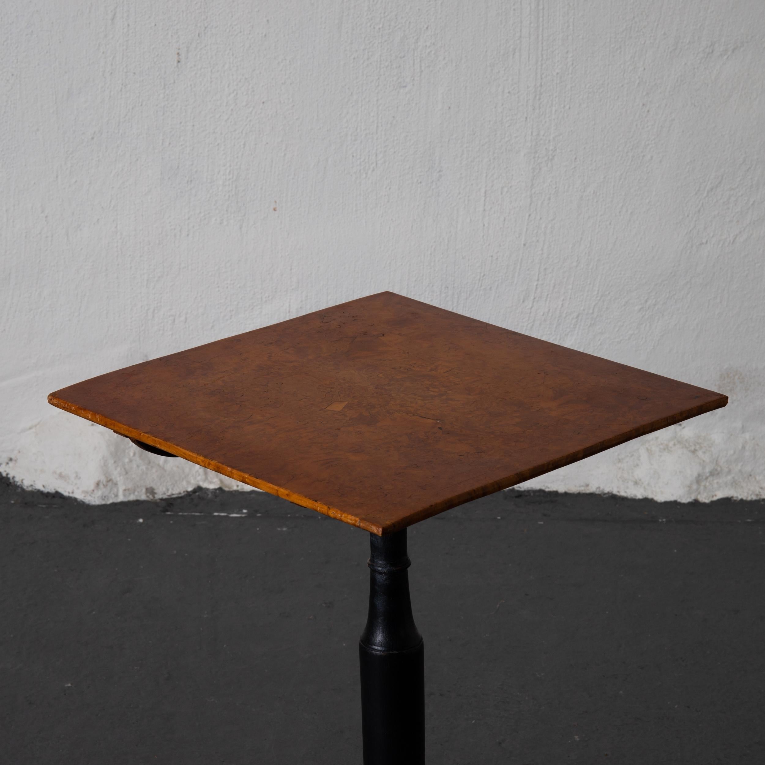 A square tilt-top table made during the 18th century in Mälardalen, Sweden. A square top made in alder root veneer. Standing on a center foot in blackened wood on a tripod base. 

  
