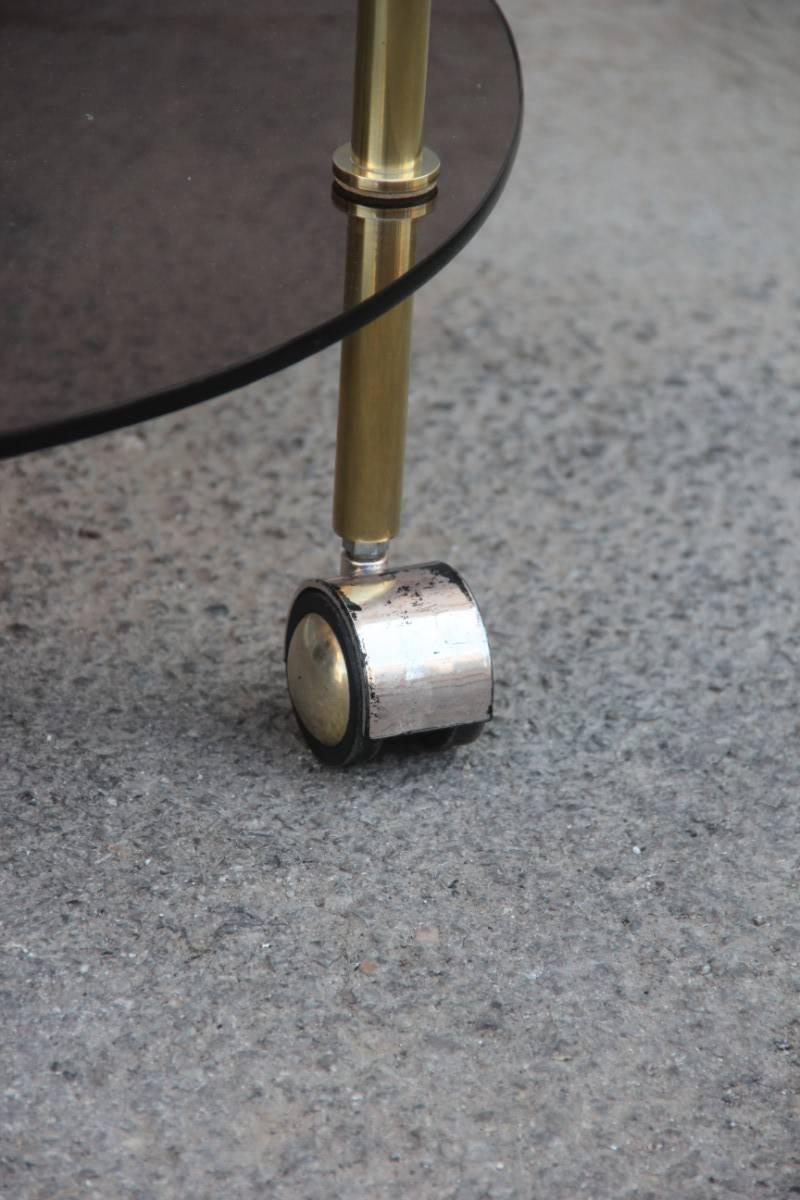 Round brass bar table and dark glasses, minimalist and delicate design, very elegant original of the 1970s. Measures: Height cm 70, diameter cm 60, the general condition is good only in the wheels left the original silver plated, due in their time